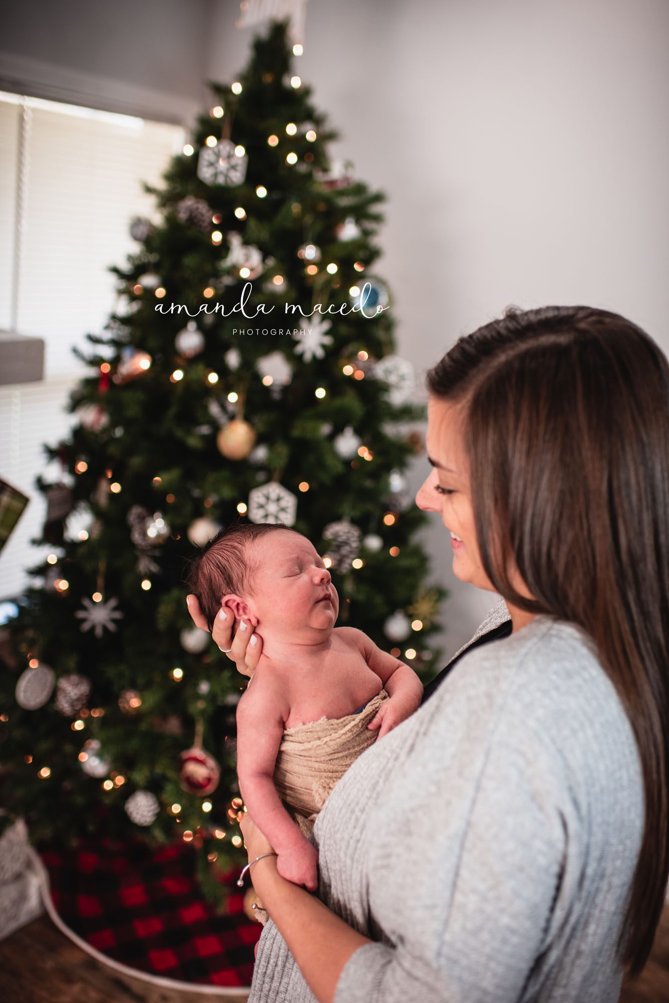 Newborn photographer, mother holding newborn baby by Christmas tree