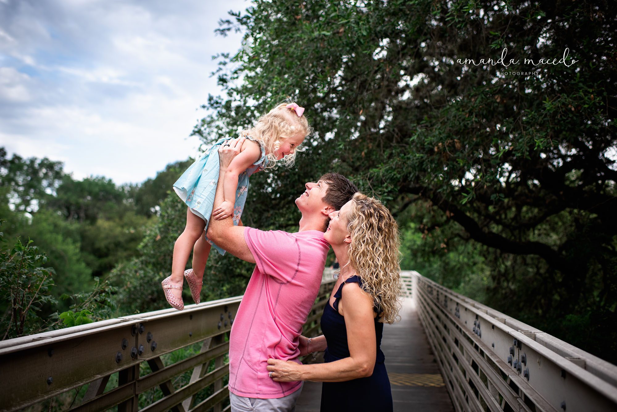 Family Photographer, Parents playing with daughter on a bridge with oak trees