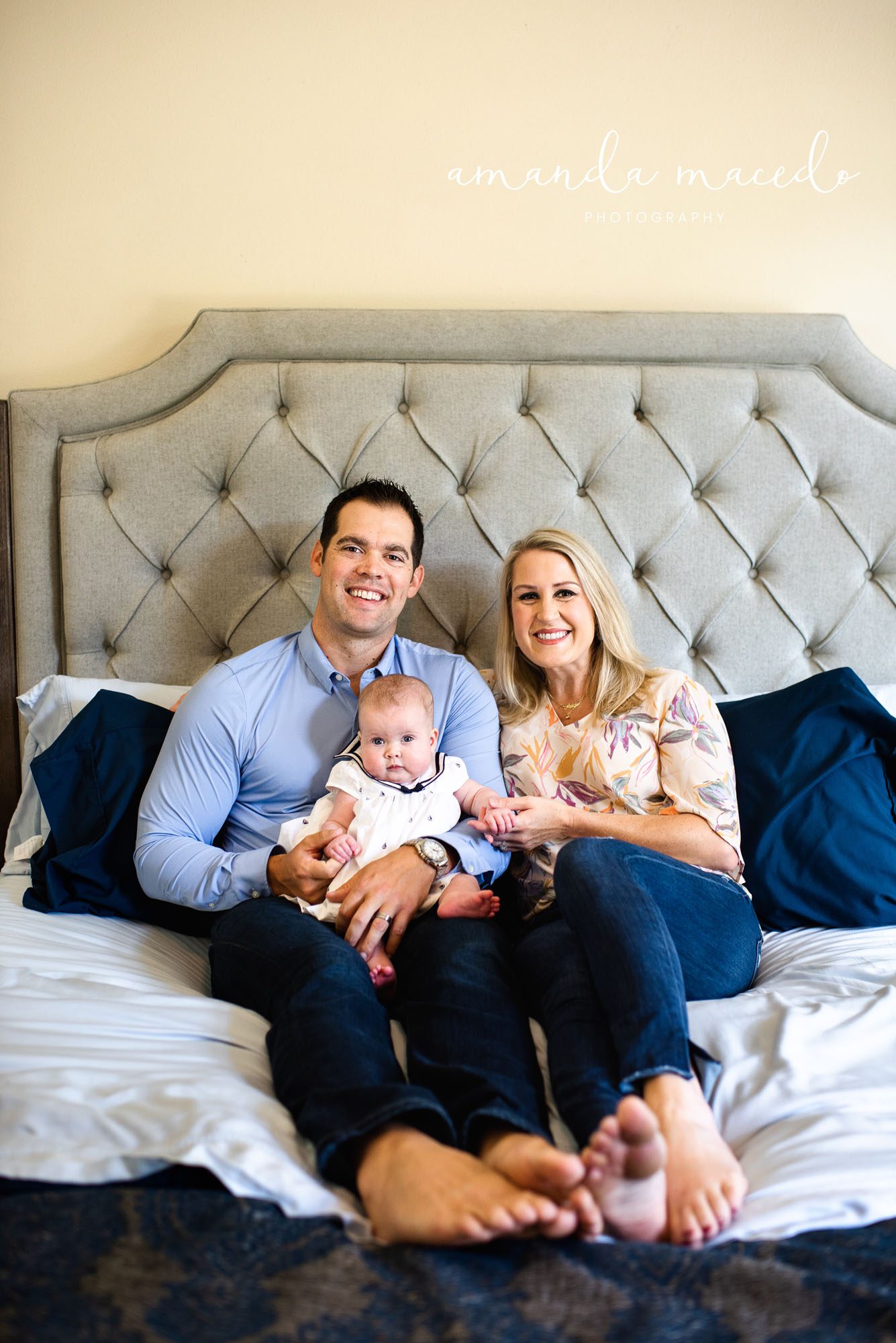 Family Photographer, parents holding baby on the bed