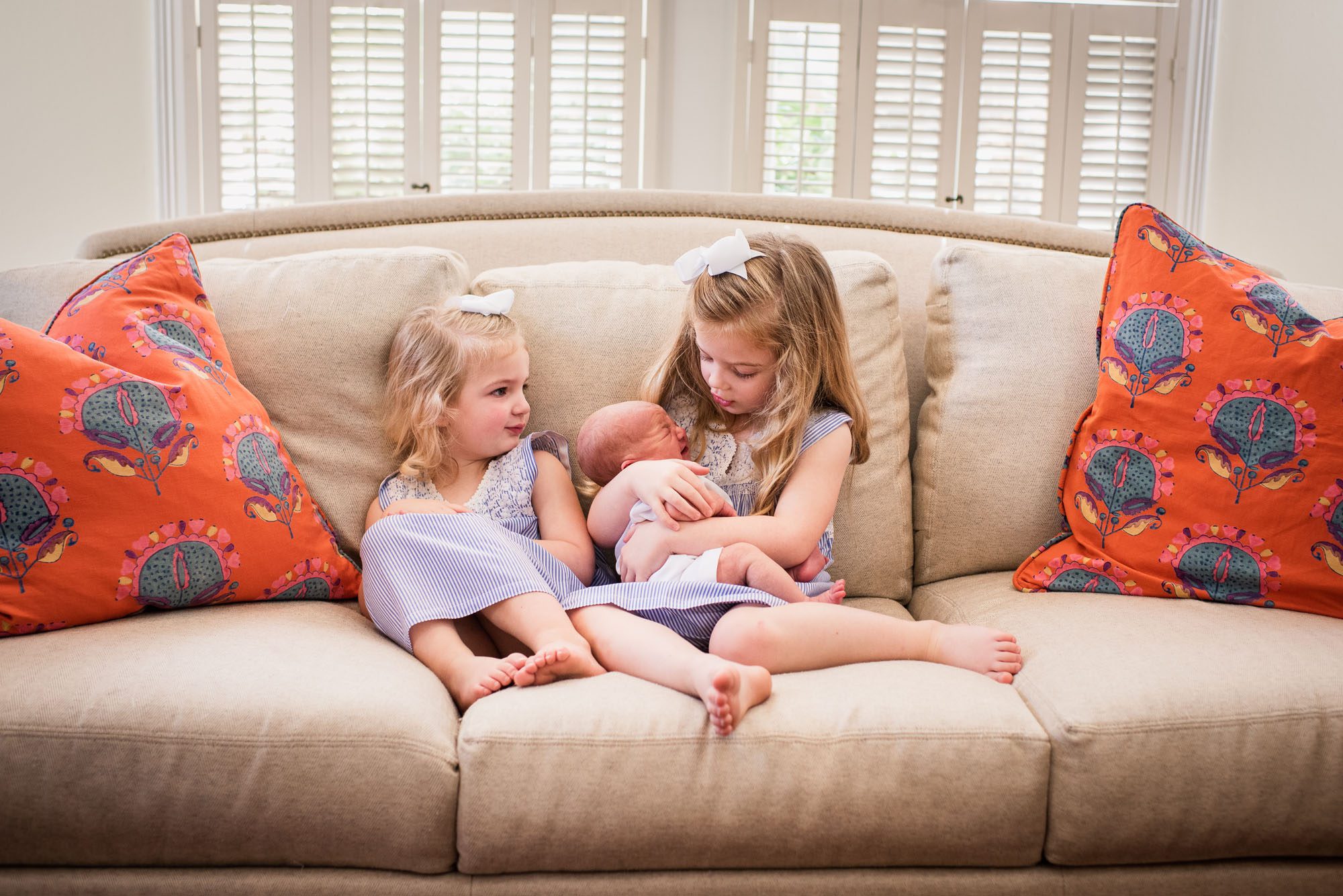 Newborn photographer, sisters on couch with newborn baby
