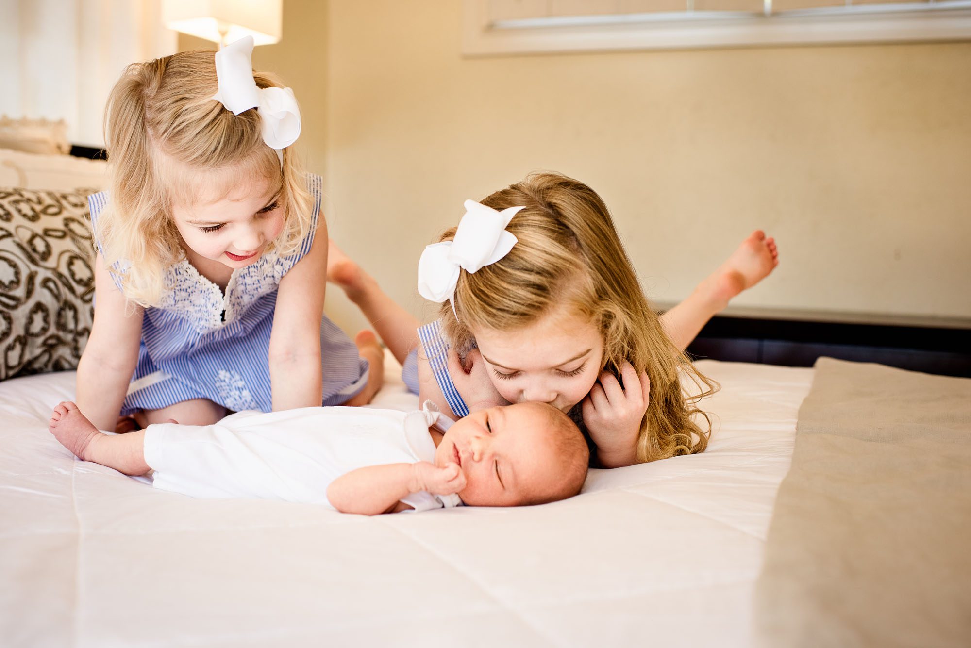 Newborn photographer, sisters on bed with newborn baby brother