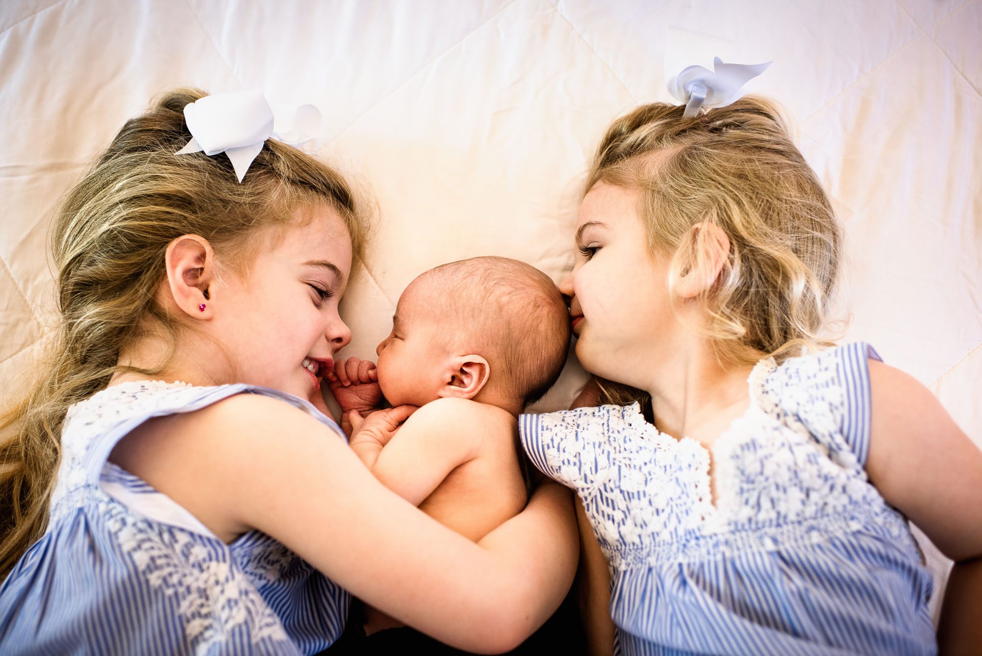 Newborn photographer, sisters laying on bed with baby brother