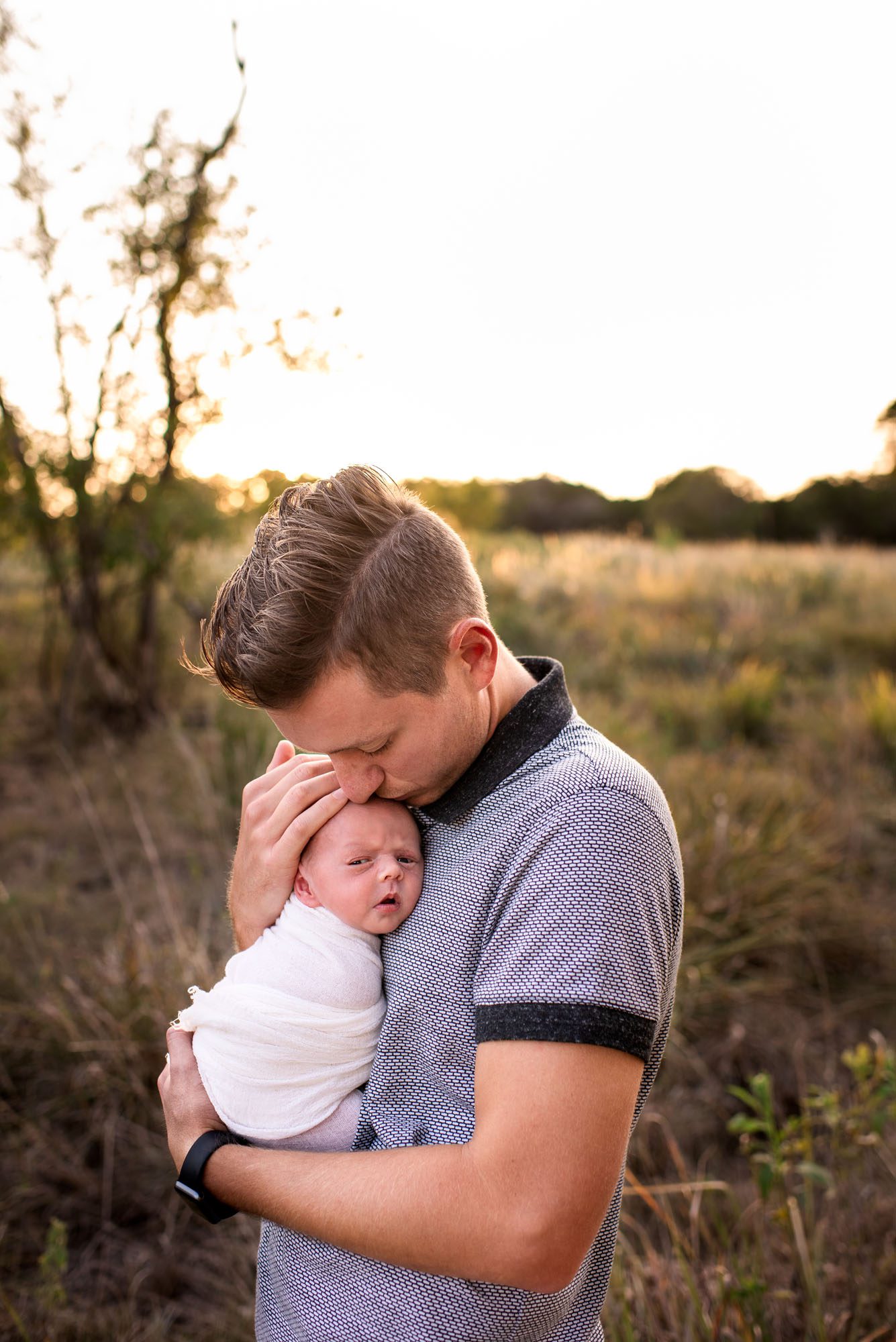 Newborn photographer, father holding newborn baby at sunset