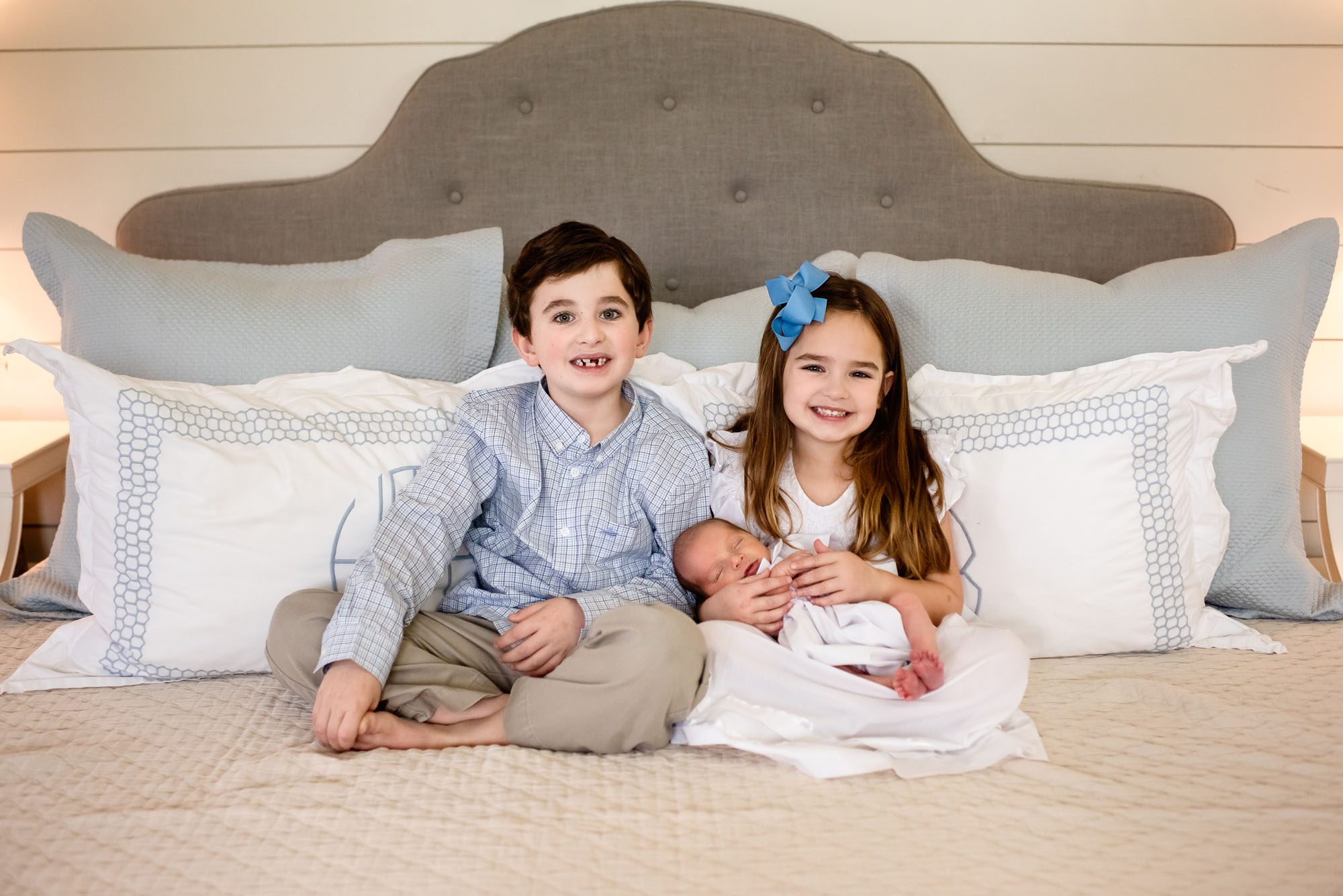 Siblings holding newborn baby on bed, San Antonio newborn photographer