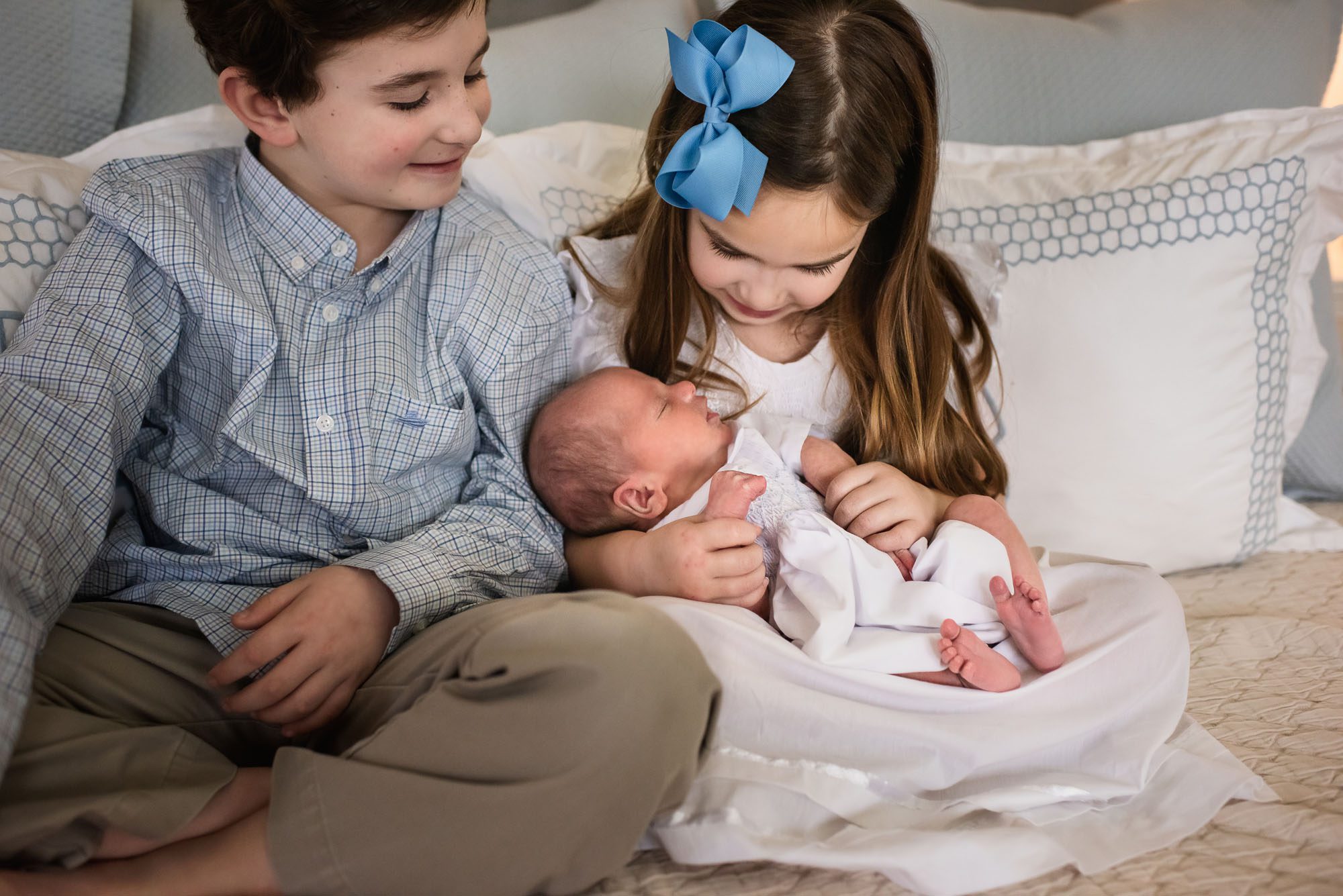 Siblings holding newborn baby on bed, San Antonio lifestyle newborn photographer