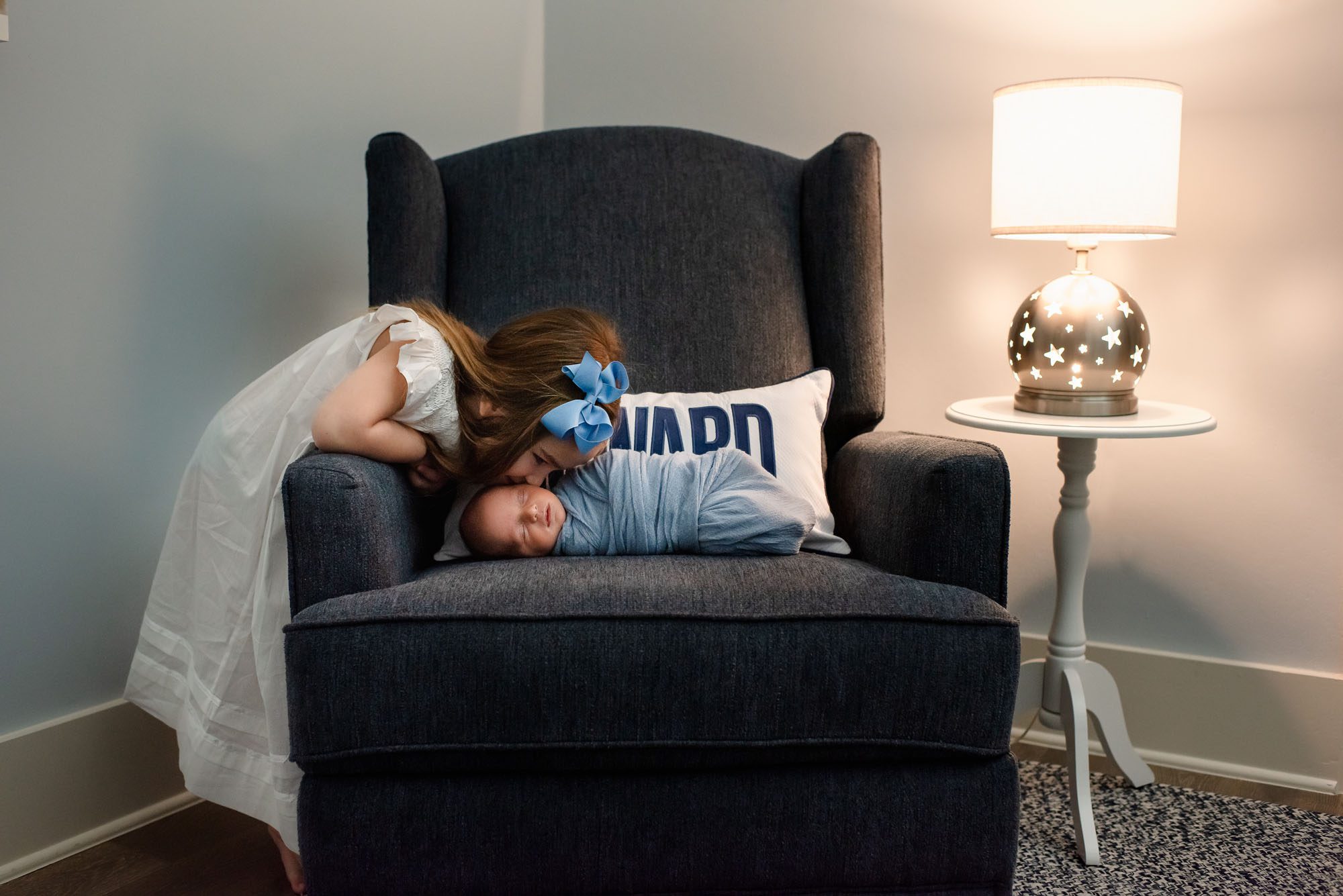 Big sister peeking over chair to kiss newborn brother, San Antonio lifestyle newborn photographer