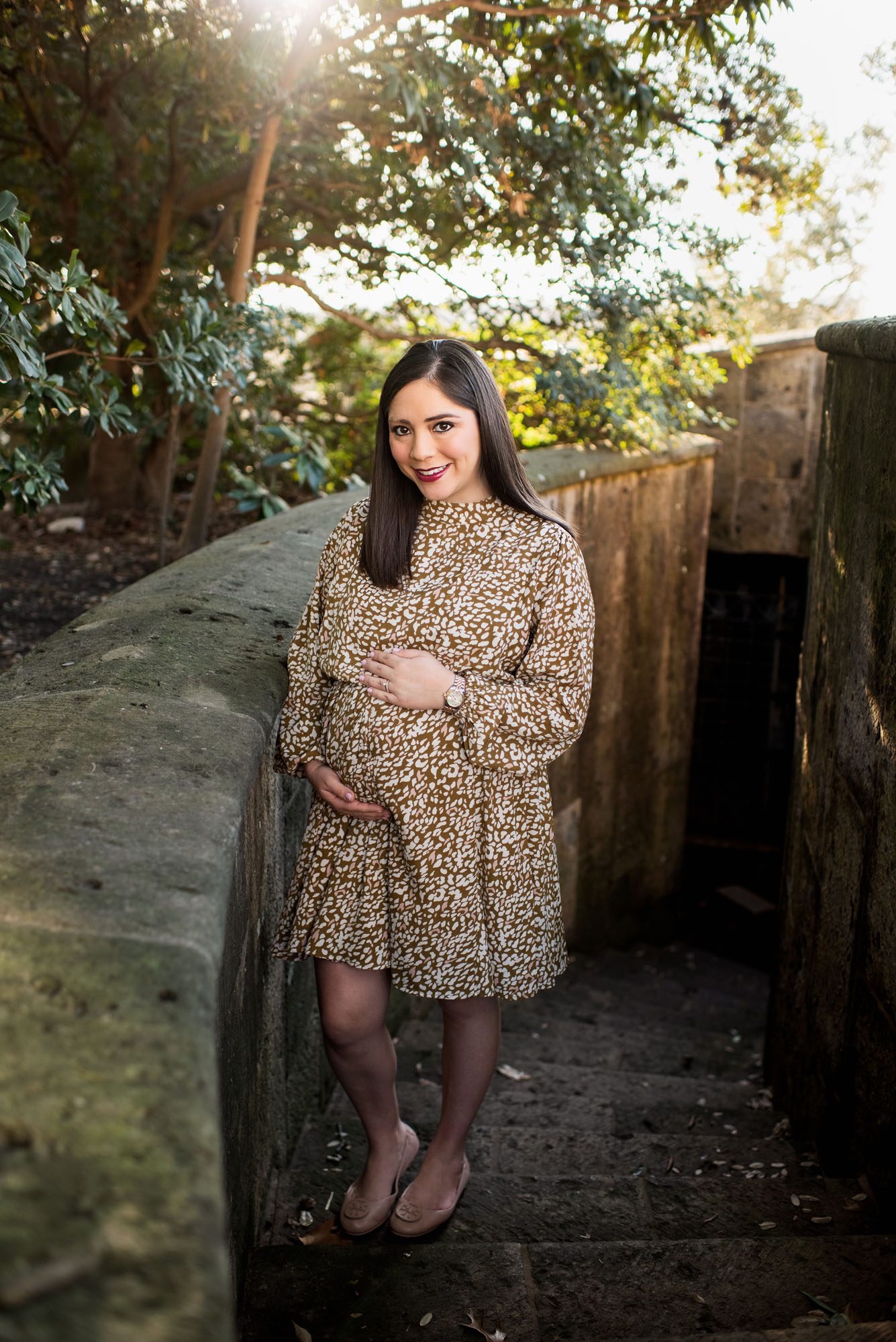 Pregnant mother standing in stairwell with sun streaming through the trees, Best San Antonio maternity photographer