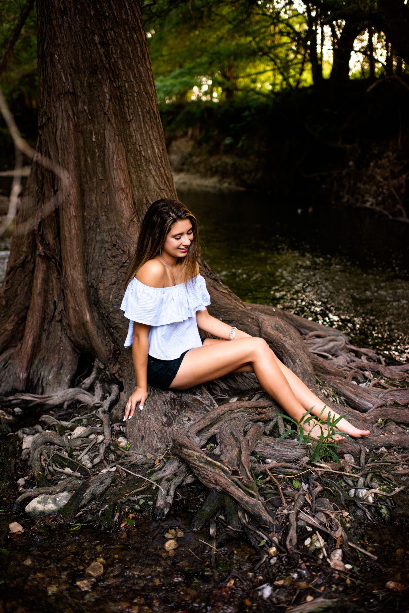 Senior girl sitting on tree roots in shallow creek, San Antonio Senior Photographer