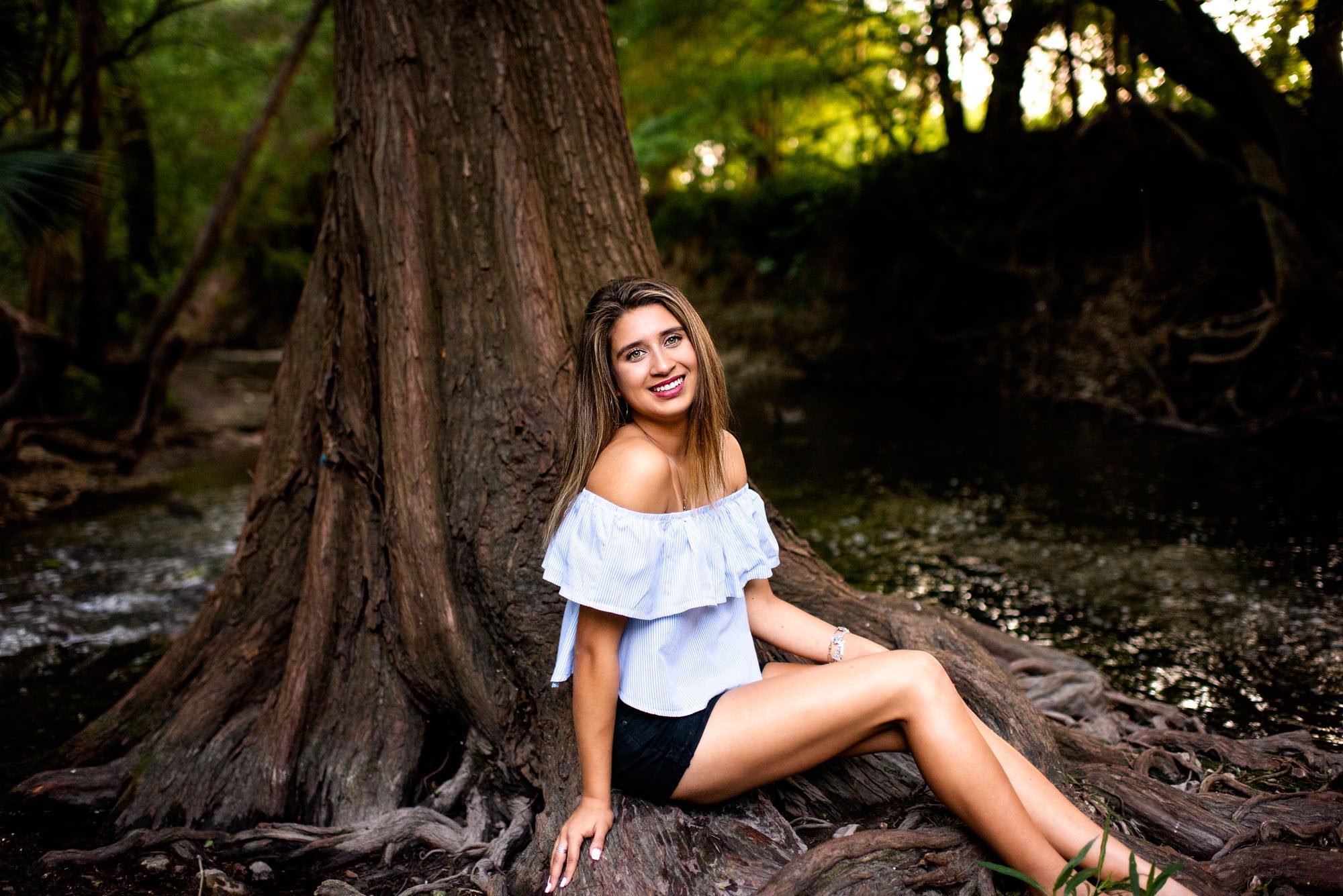 Senior girl sitting on tree roots in shallow creek, San Antonio Senior Photographer