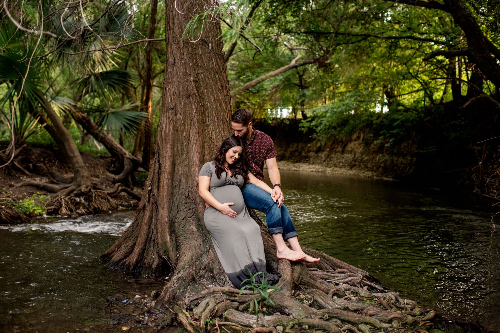 Pregnant couple sitting on tree trunk in creek at sunset, San Antonio Maternity Photographer