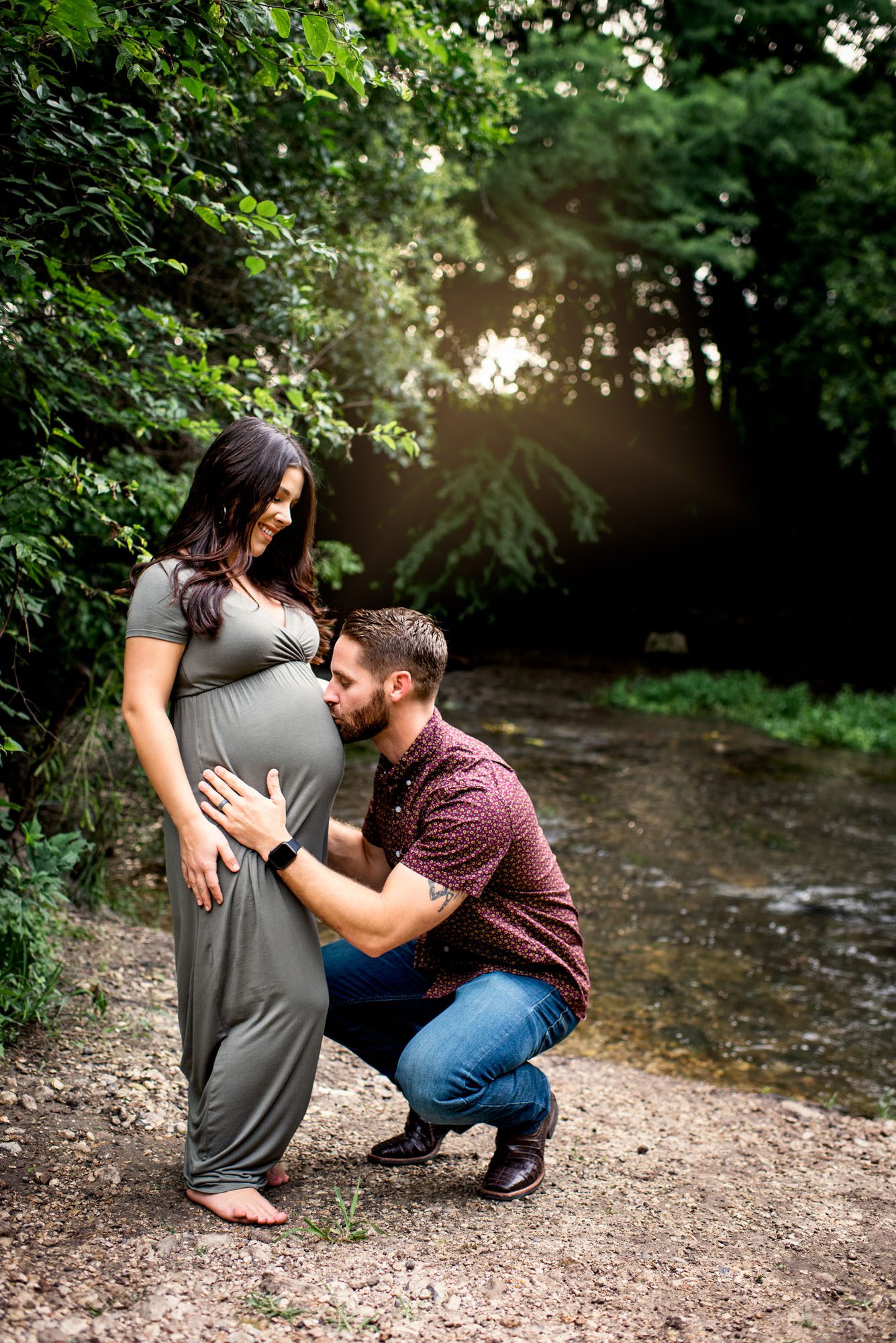 Husband kissing wife's pregnant belly near creek at sunset, San Antonio Maternity Photographer