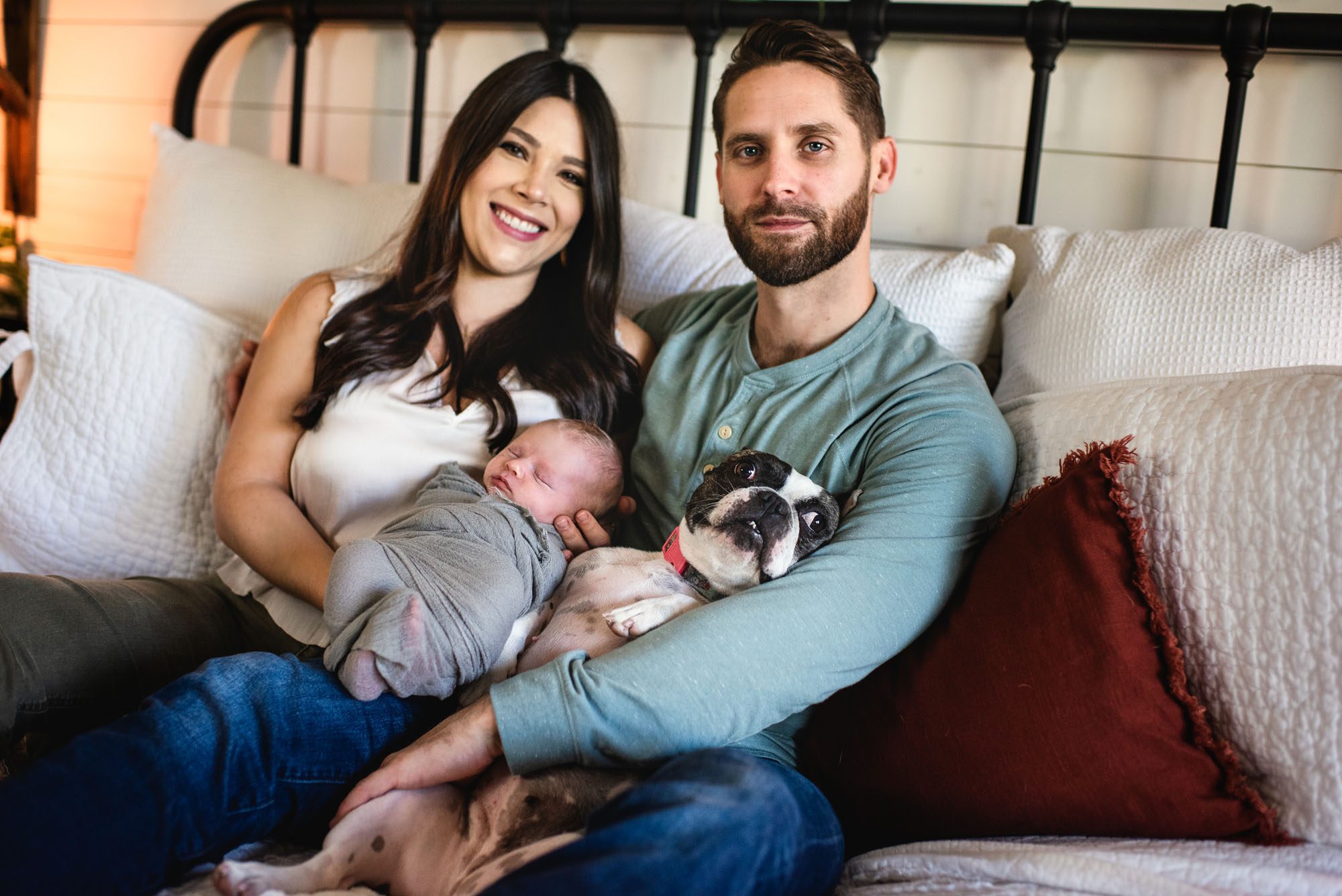 Newborn Photographer in San Antonio, Couple holding newborn baby on bed with dog