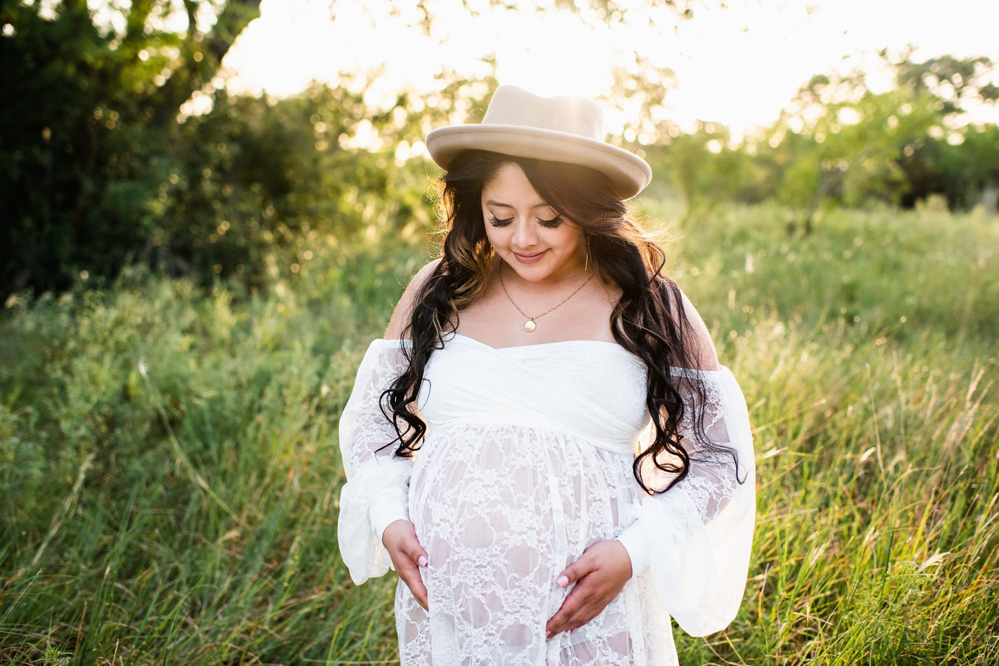 Expectant mother smiling and looking at her belly in a field, San Antonio maternity photography
