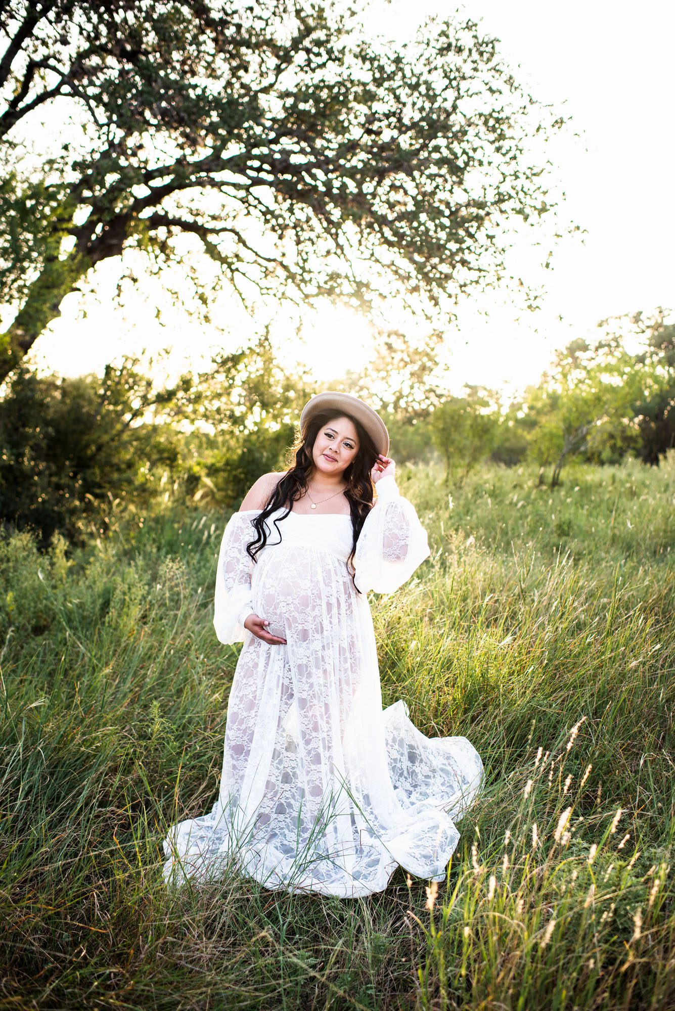 Expectant mother in white dress and hat at sunset in a field, San Antonio maternity session