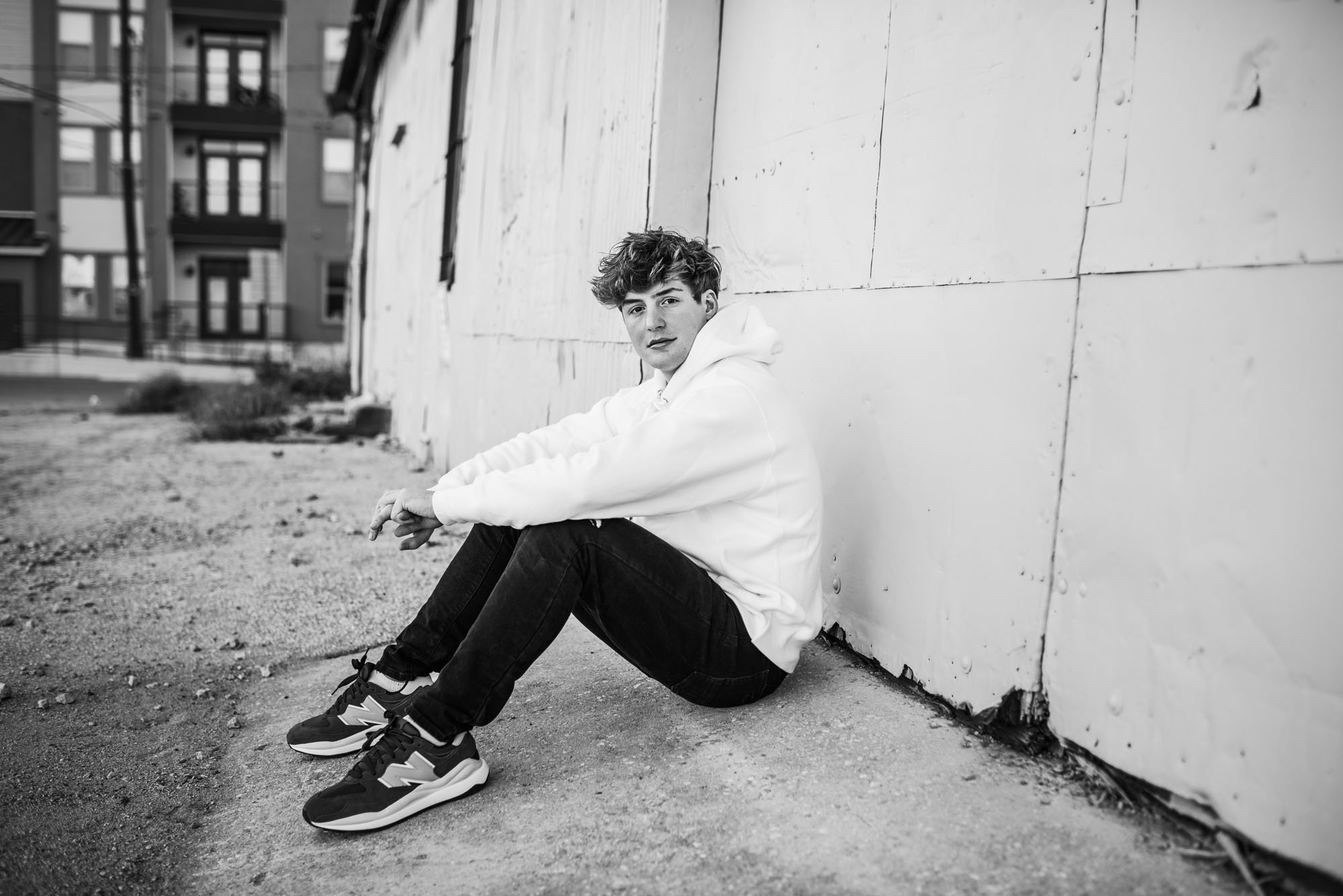 Senior Photographer San Antonio, black and white image of boy sitting by warehouse wall