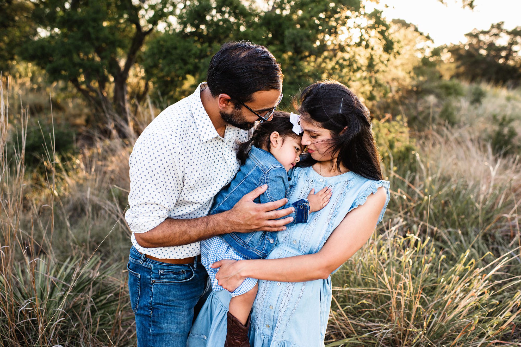 Parents hugging daughter in field, San Antonio area family photographer