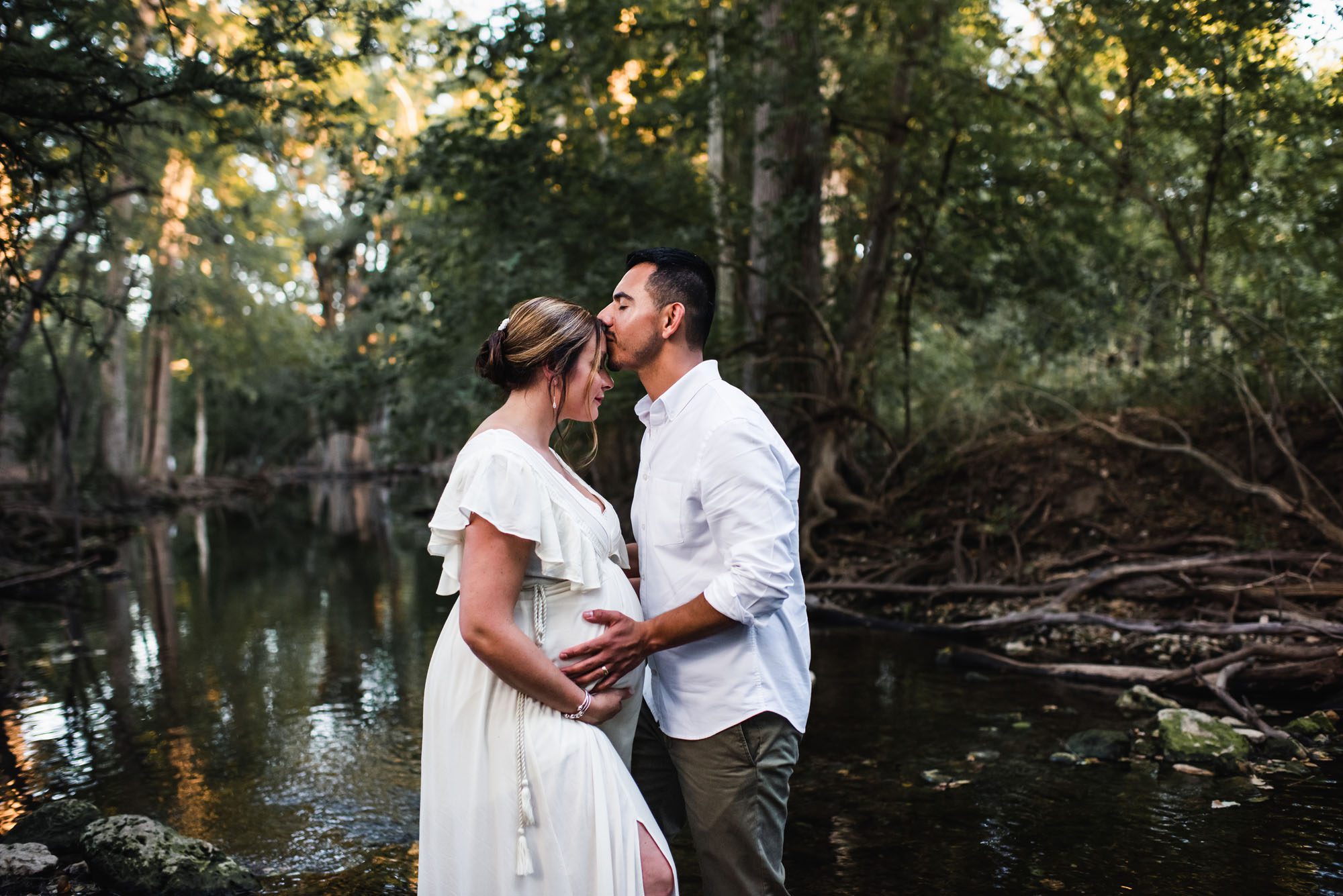 San Antonio lifestyle maternity photographer, husband kissing pregnant wife's forehead in creek
