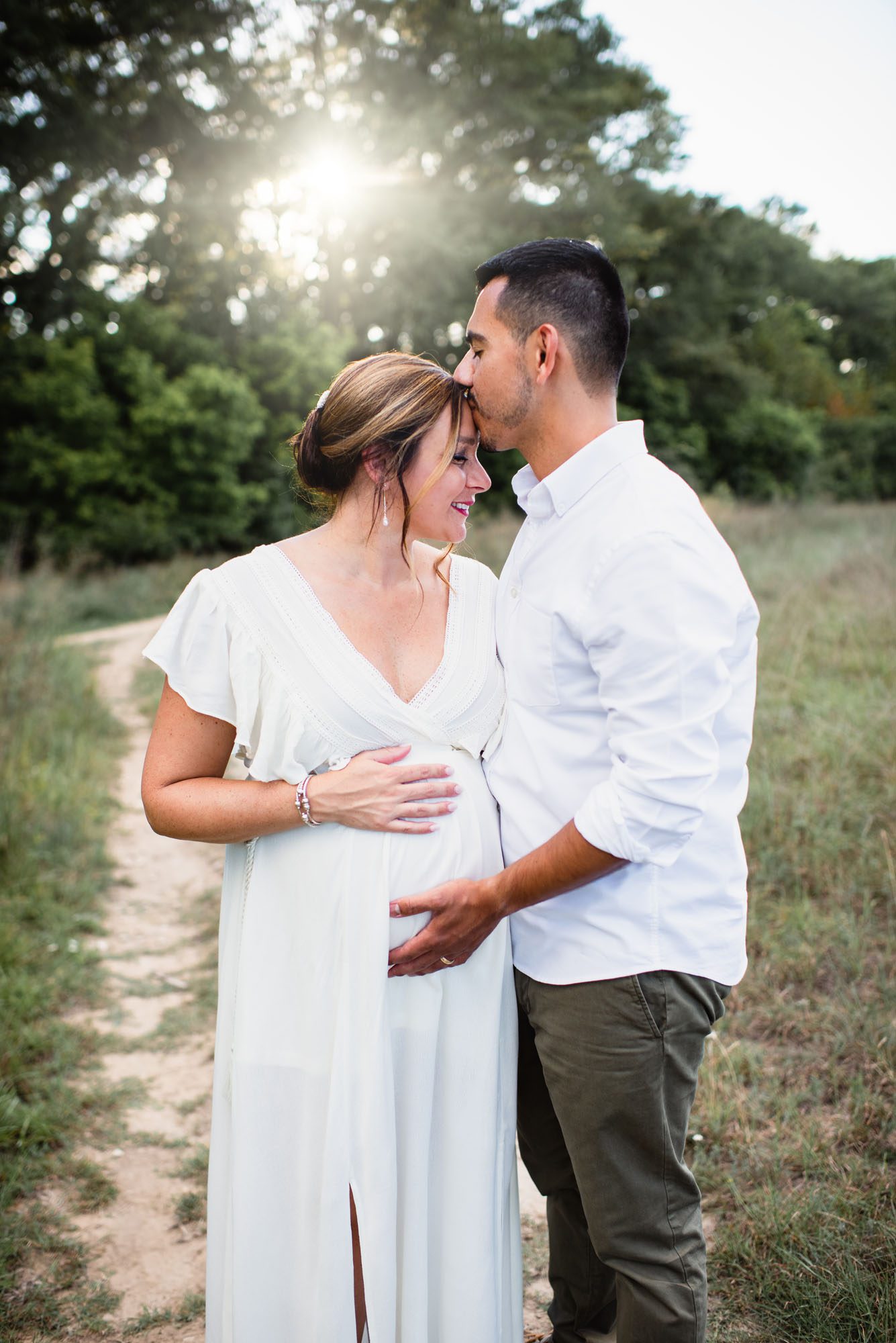 Husband kissing pregnant wife's forehead in a field at sunset, San Antonio maternity photographer