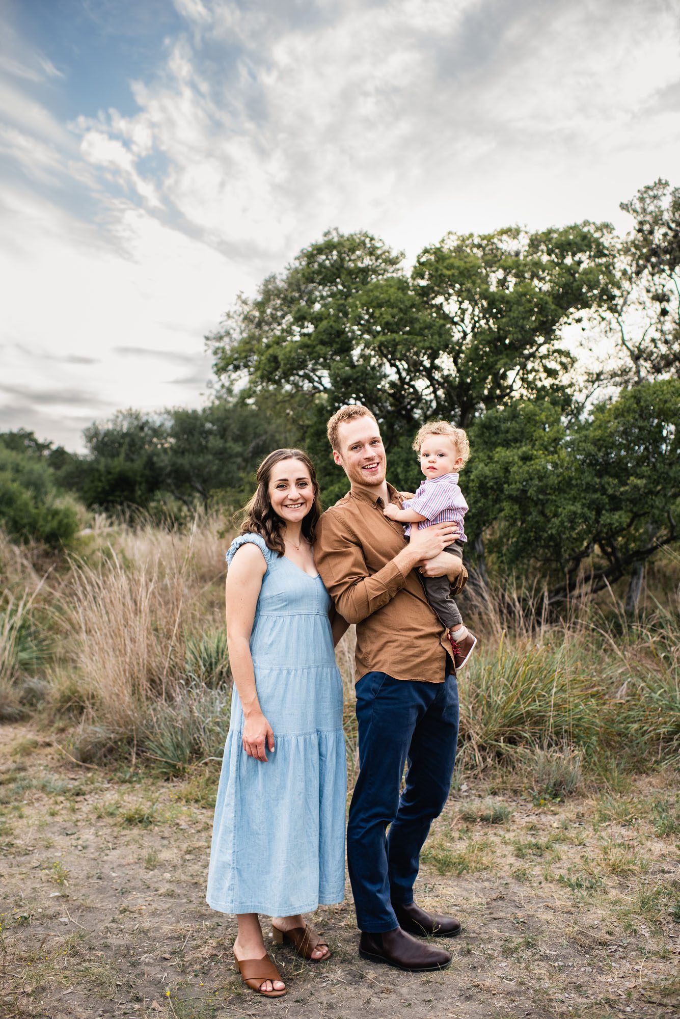 Parents holding baby boy in a field with cloudy sky, San Antonio Family Photographer