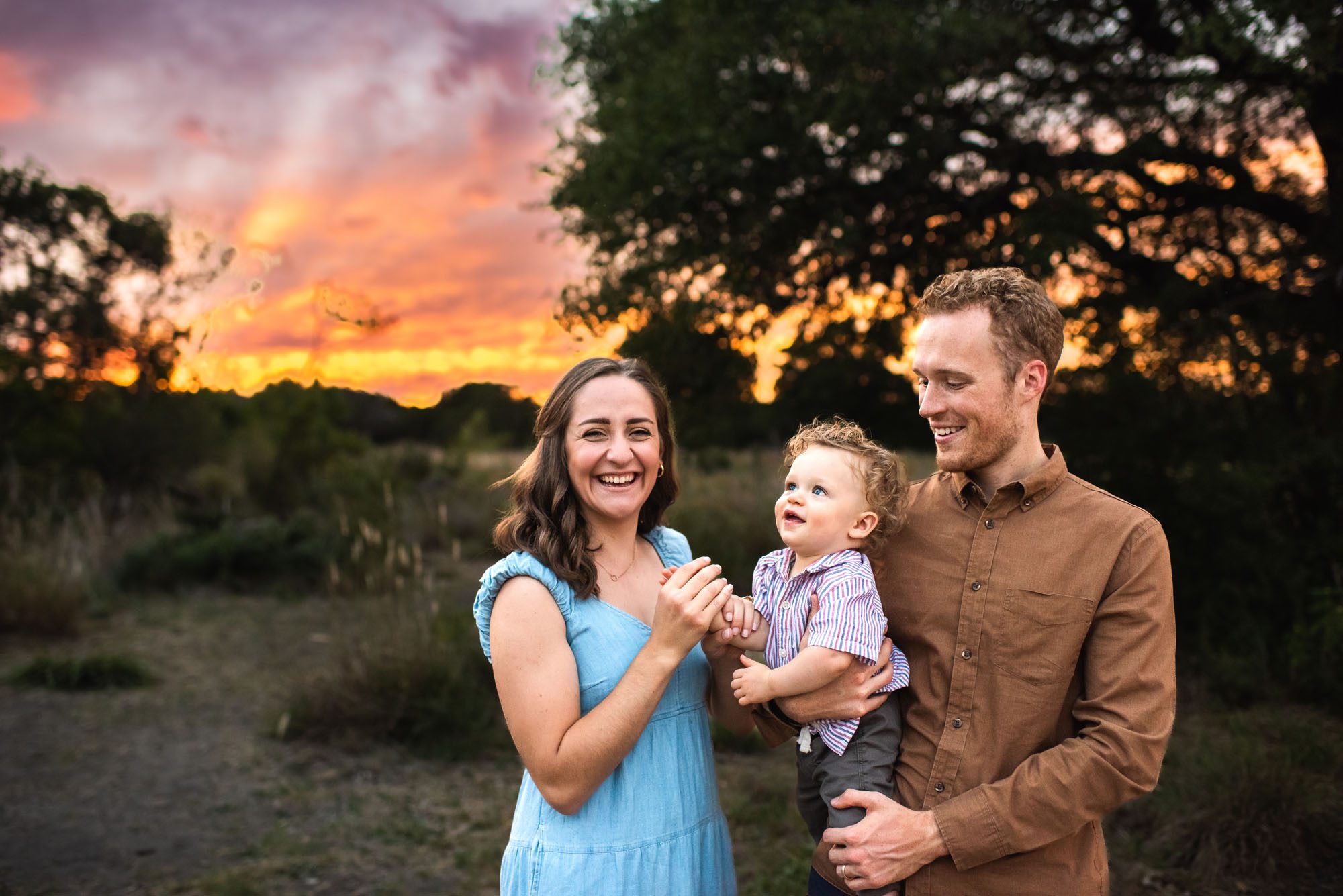 Parents playing with baby boy in field with colorful sunset, San Antonio Family Photographer