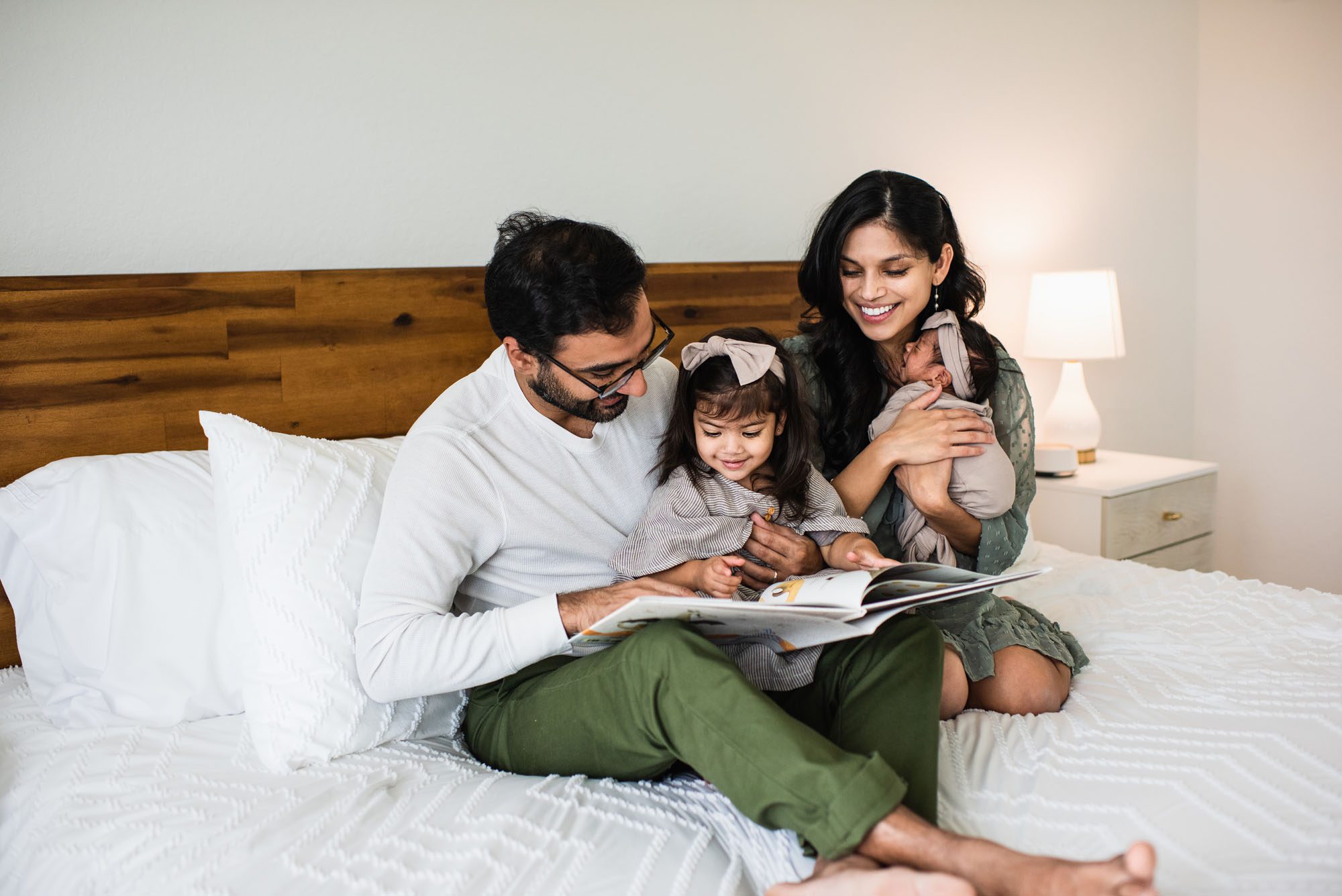 Family smiling while reading a book on bed, San Antonio lifestyle newborn photographer