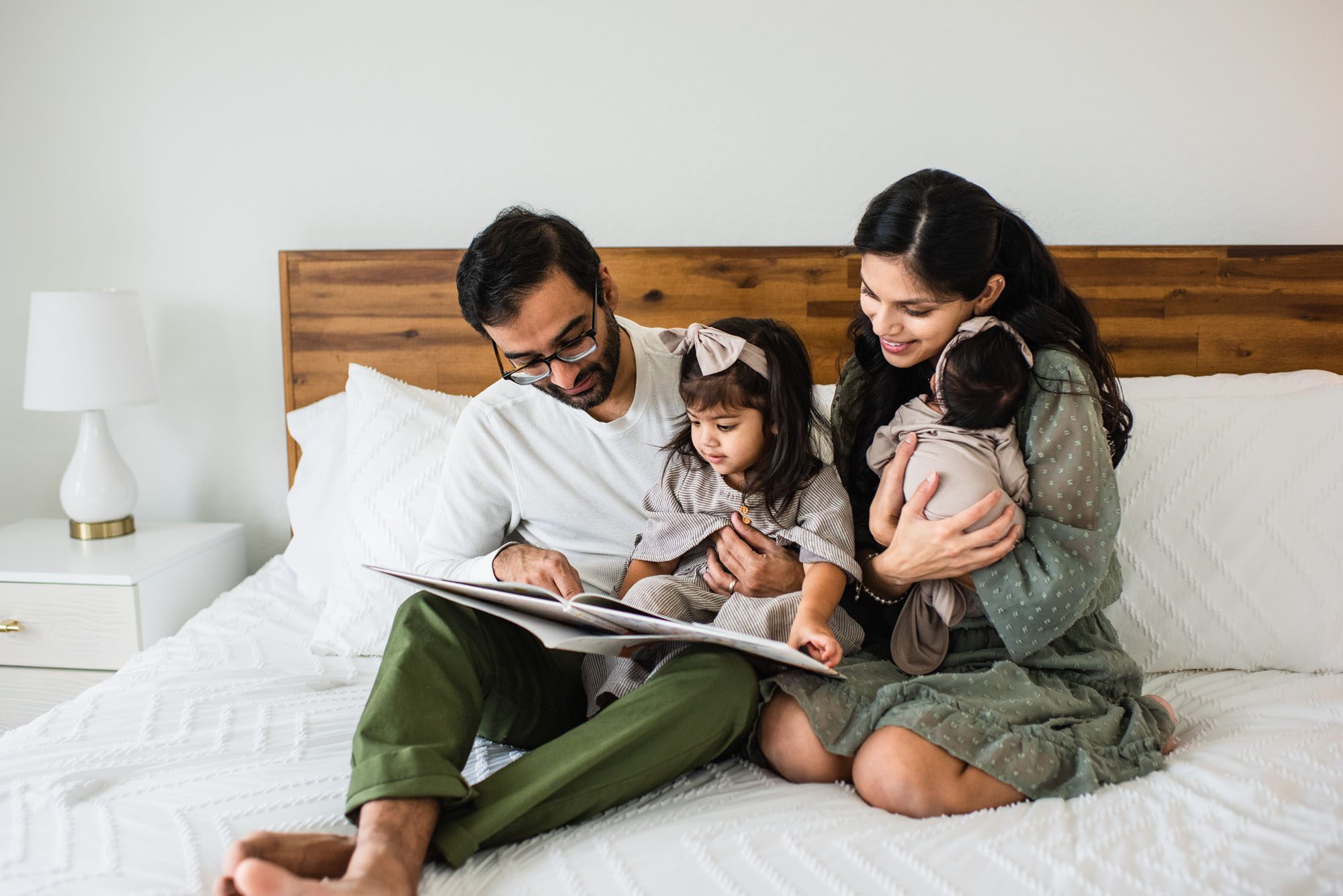 Family reading a book on bed with newborn baby, San Antonio lifestyle newborn photographer