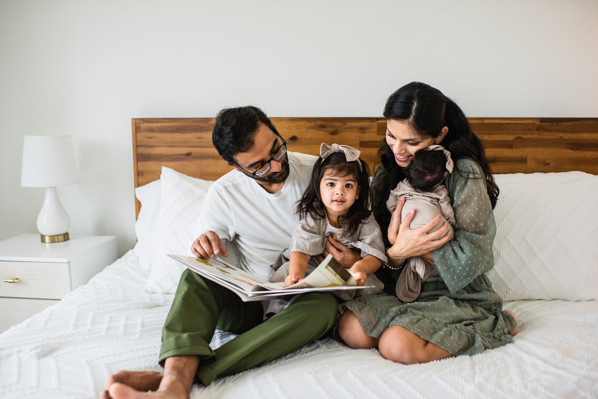 Family reading a book on bed with newborn baby, San Antonio lifestyle newborn photographer