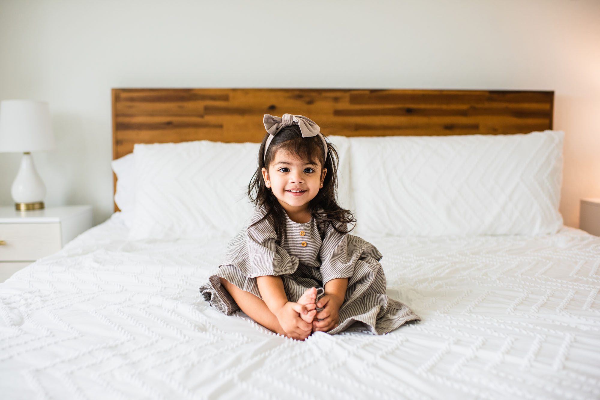 Little girl sitting on bed and smiling, San Antonio newborn photographer