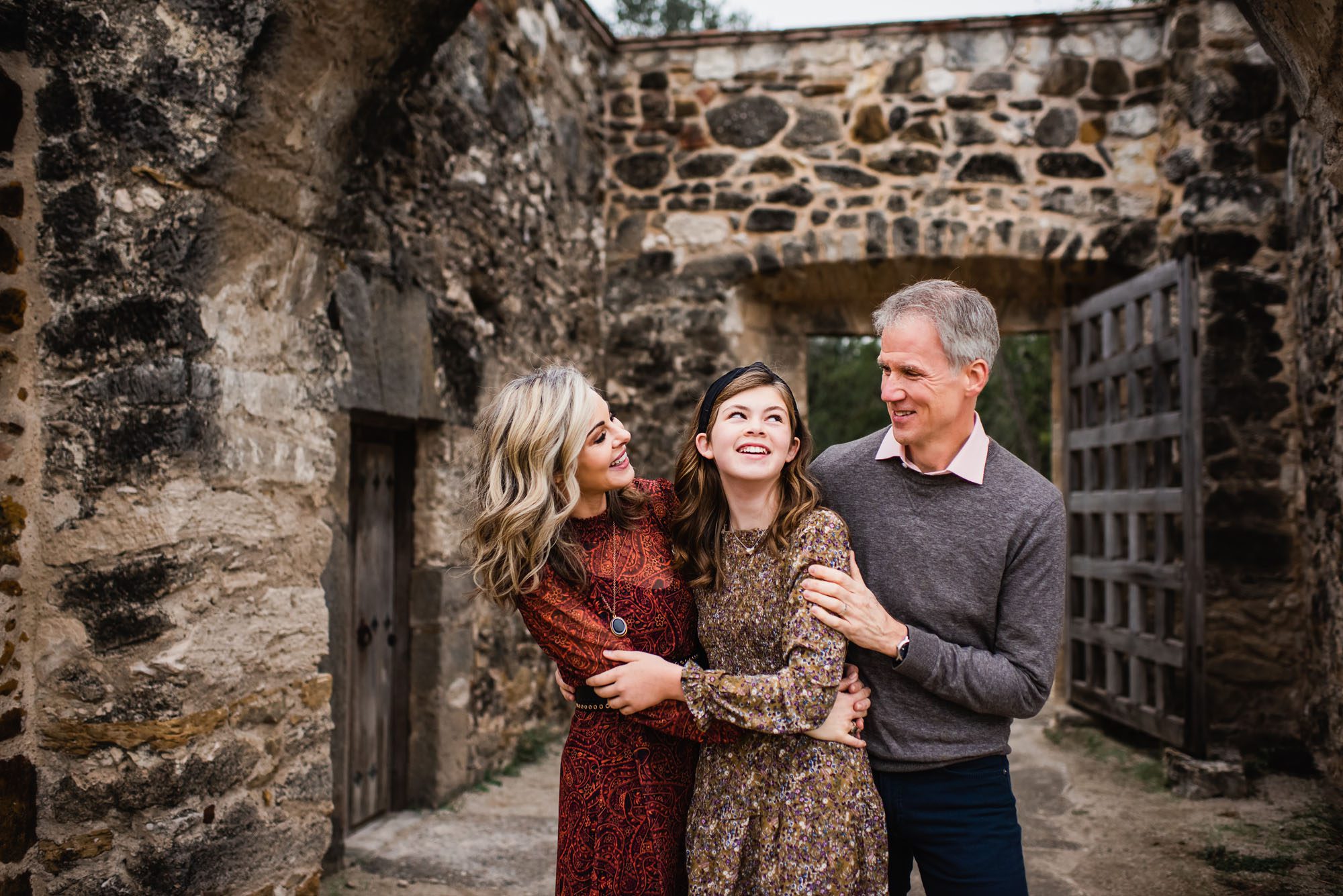 Family hugging and smiling near brown stone wall, San Antonio lifestyle photographer