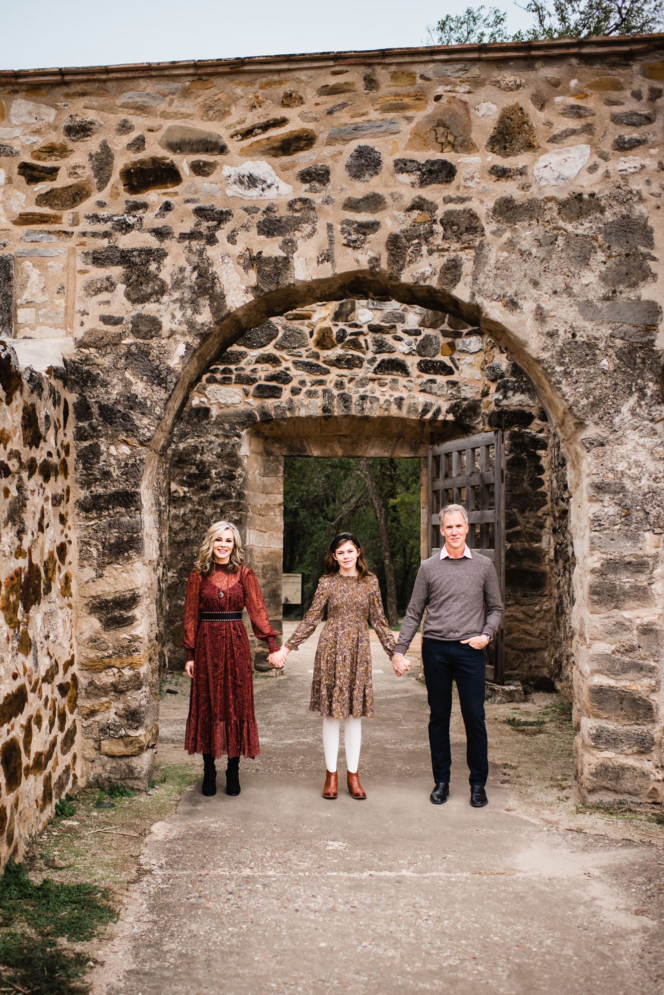 Family holding hands in front of brown stone wall, San Antonio lifestyle photographer