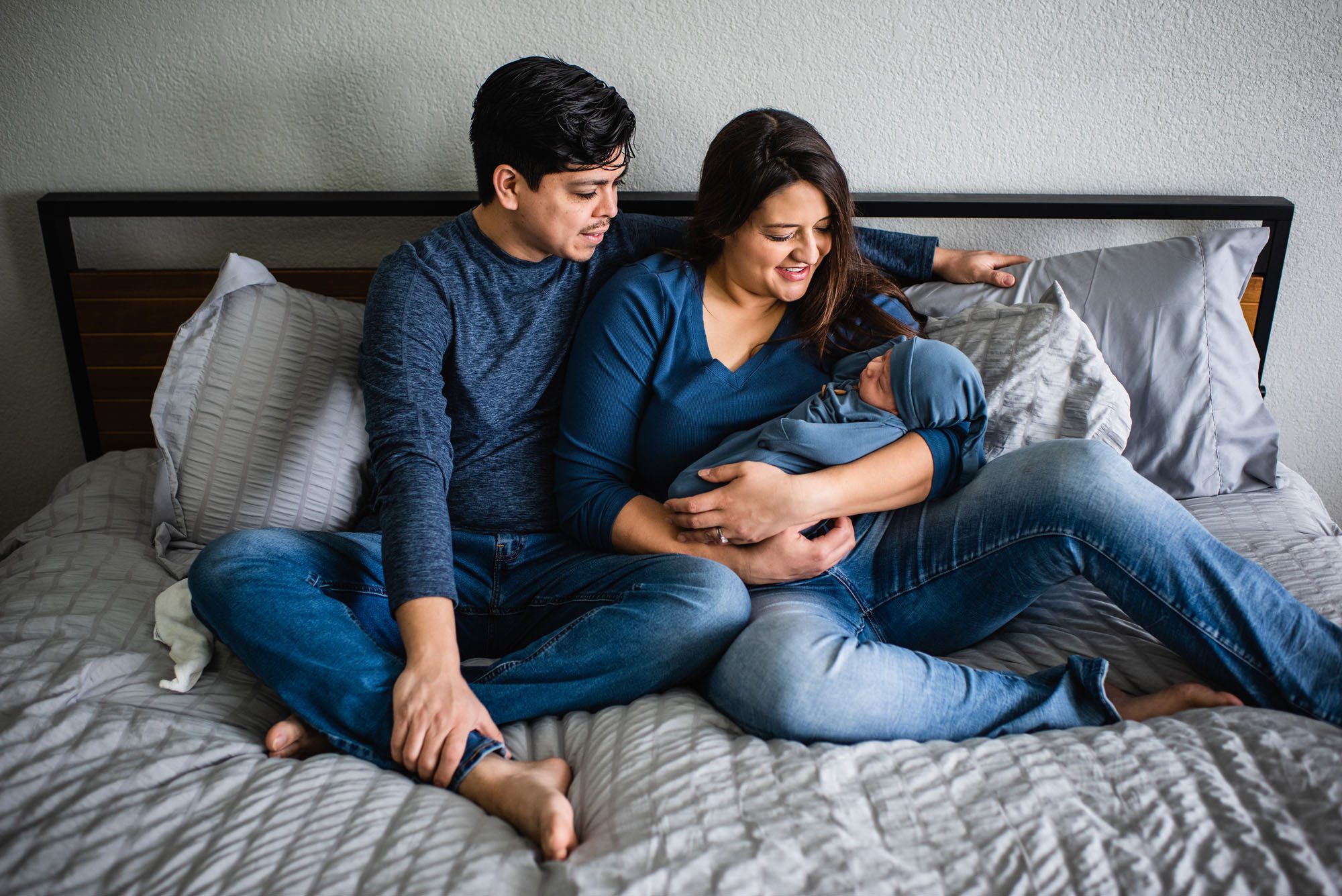 Parents sitting on bed smiling at newborn baby, San Antonio Lifestyle Newborn Photographer