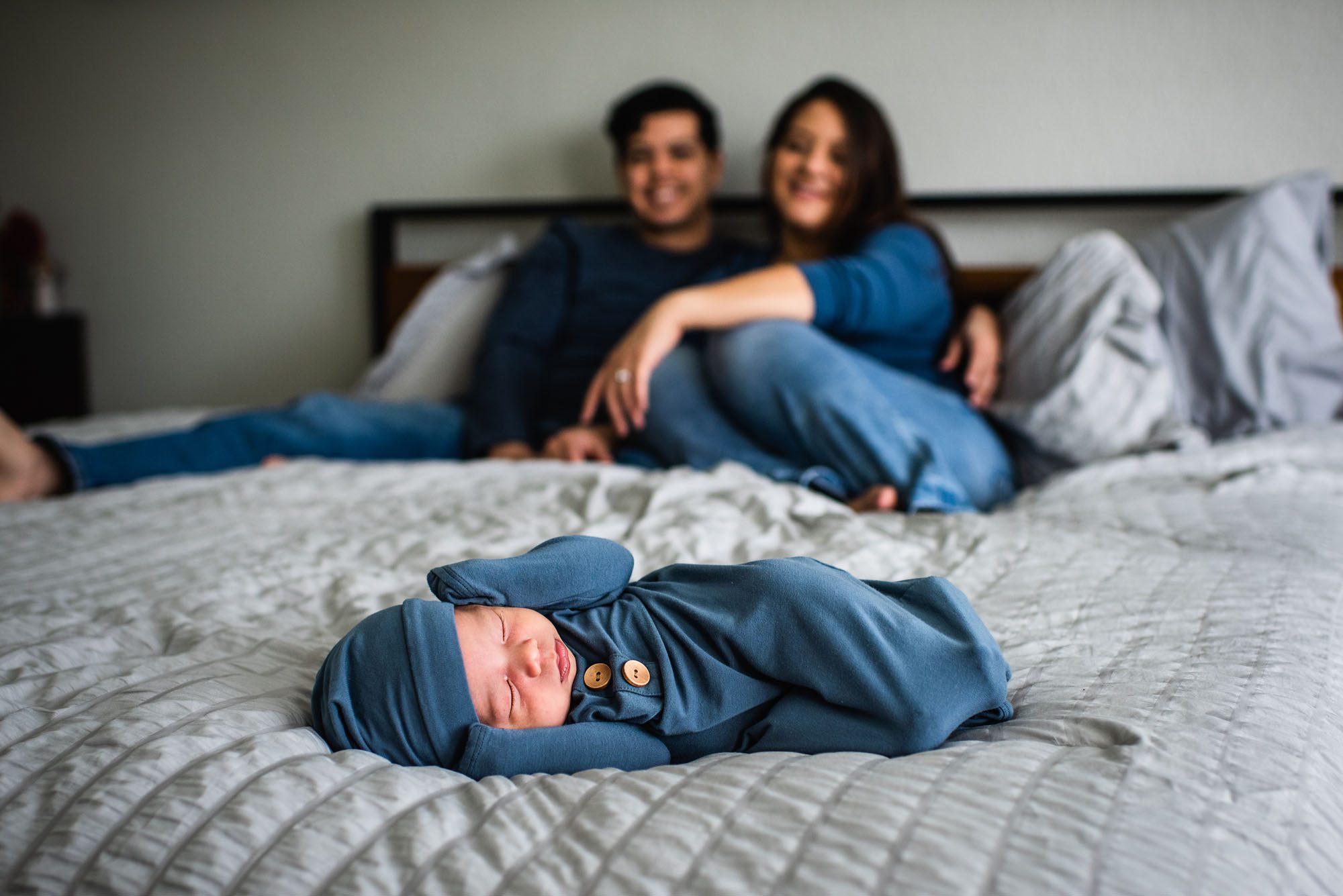 Newborn baby sleeping on bed with parents in the background, San Antonio Lifestyle Newborn Photographer