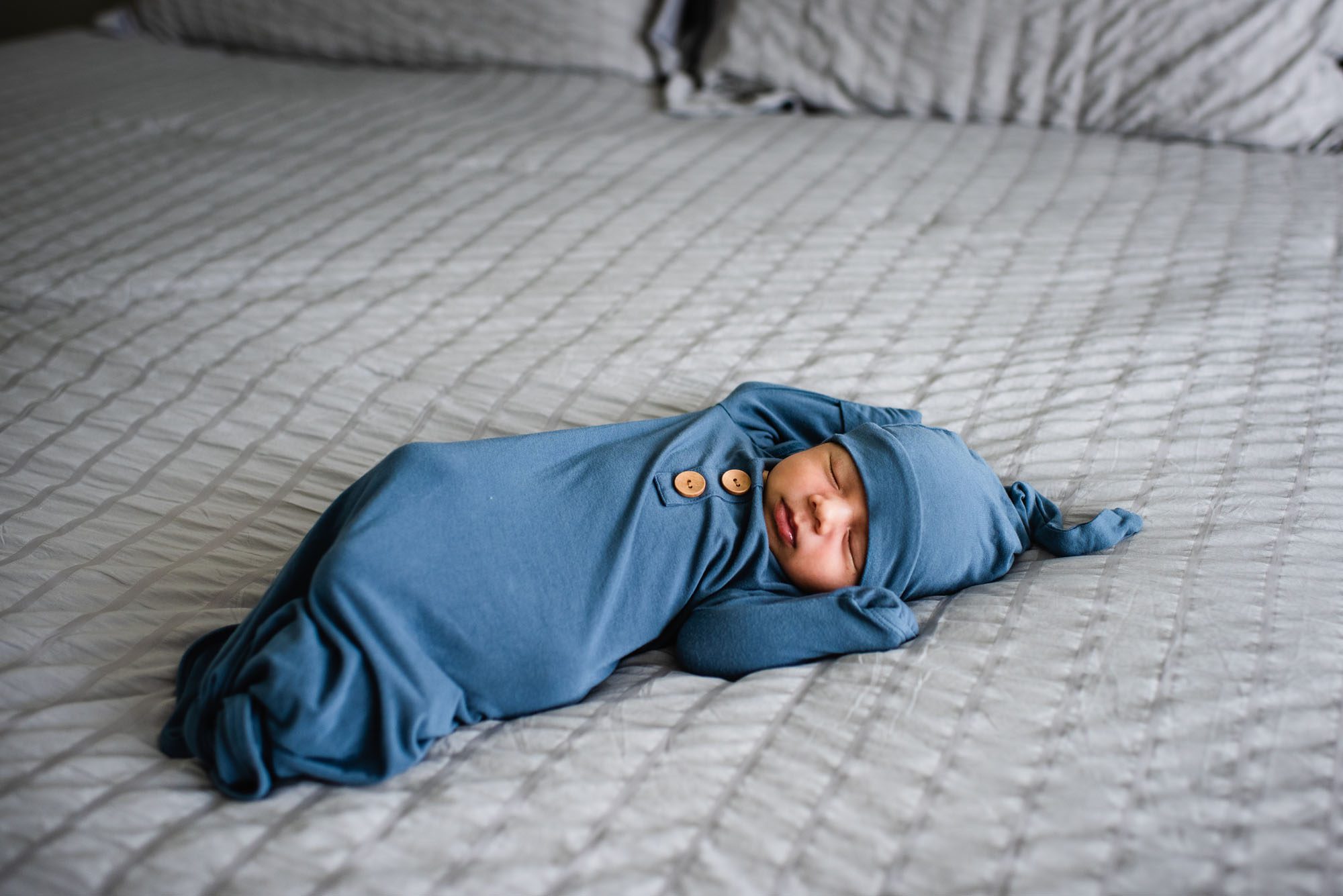 San Antonio Newborn Photographer, newborn baby laying on bed in blue sleep sack