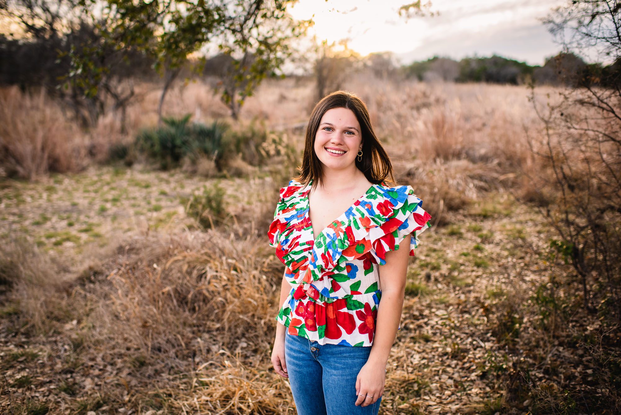 Senior girl in a brightly colored top in a field at sunset, San Antonio senior portrait photographer