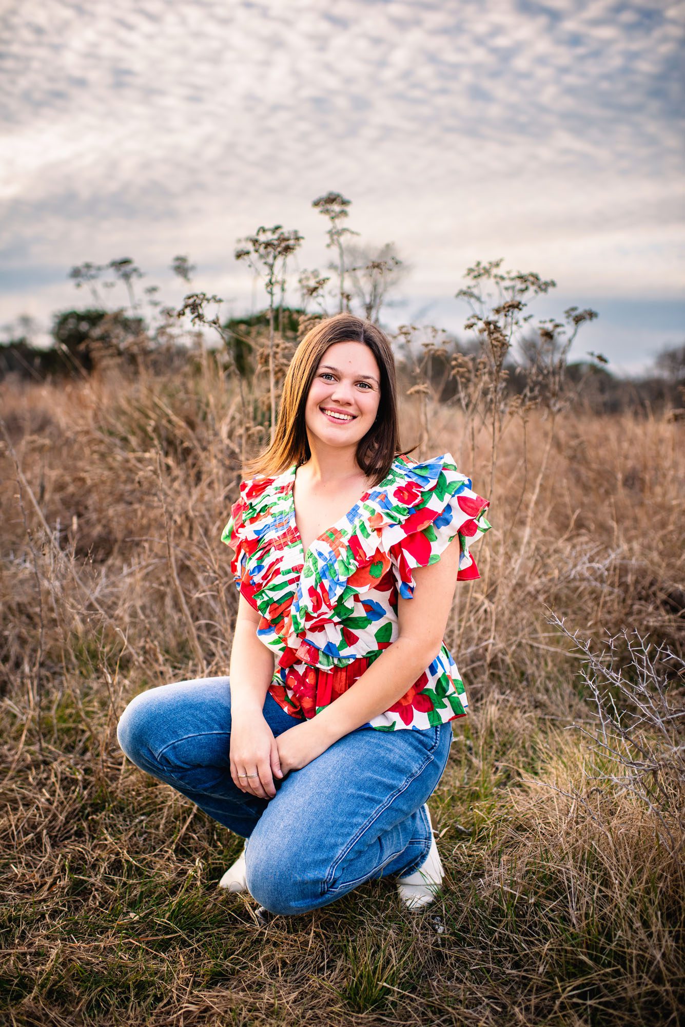 Senior girl in a brightly colored top kneeling down in a field, San Antonio senior photographer
