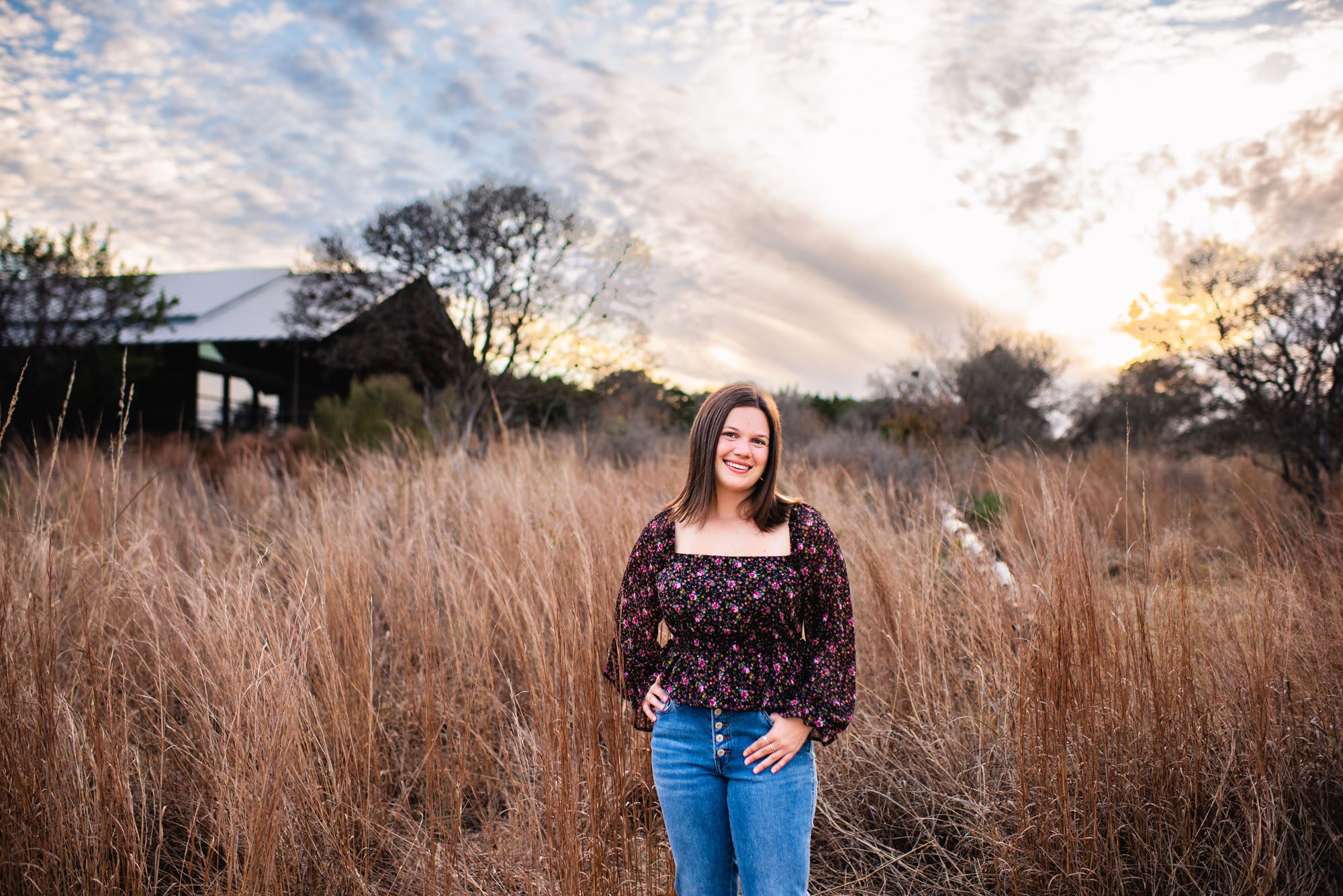 Senior girl in a grassy field with cloudy sky, San Antonio senior portrait photographer