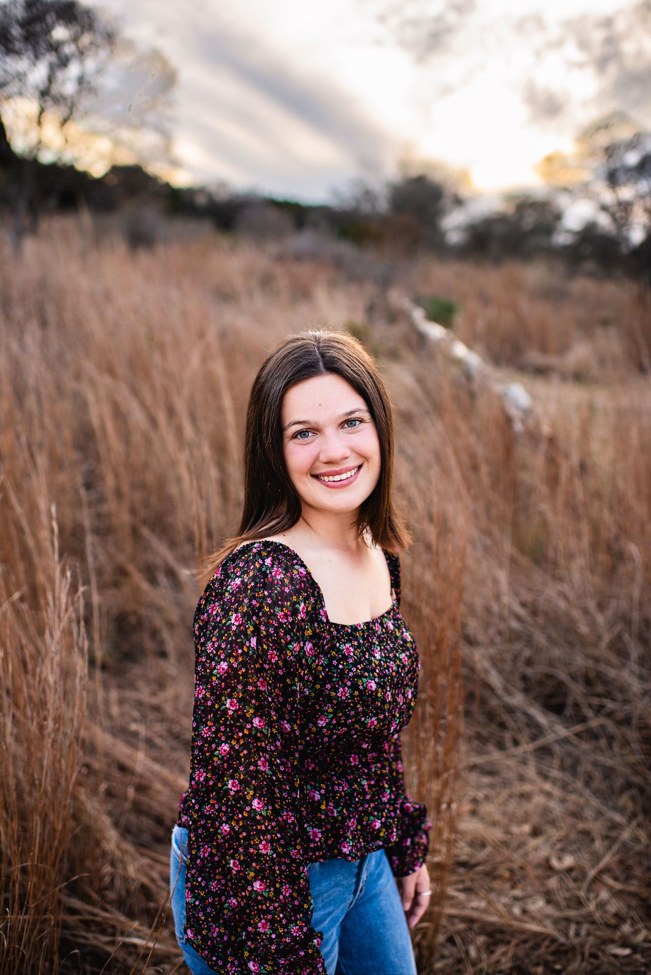 Senior girl in a field with long grasses and cloudy sky, San Antonio senior photographer