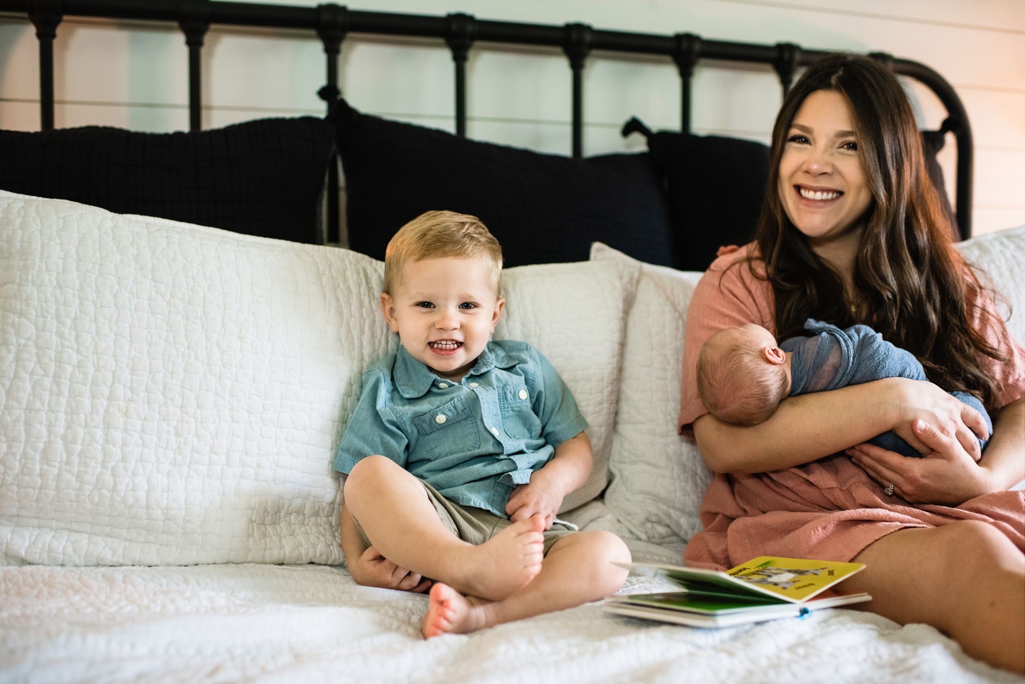 Toddler smiling on bed with mother and baby, San Antonio newborn photographer