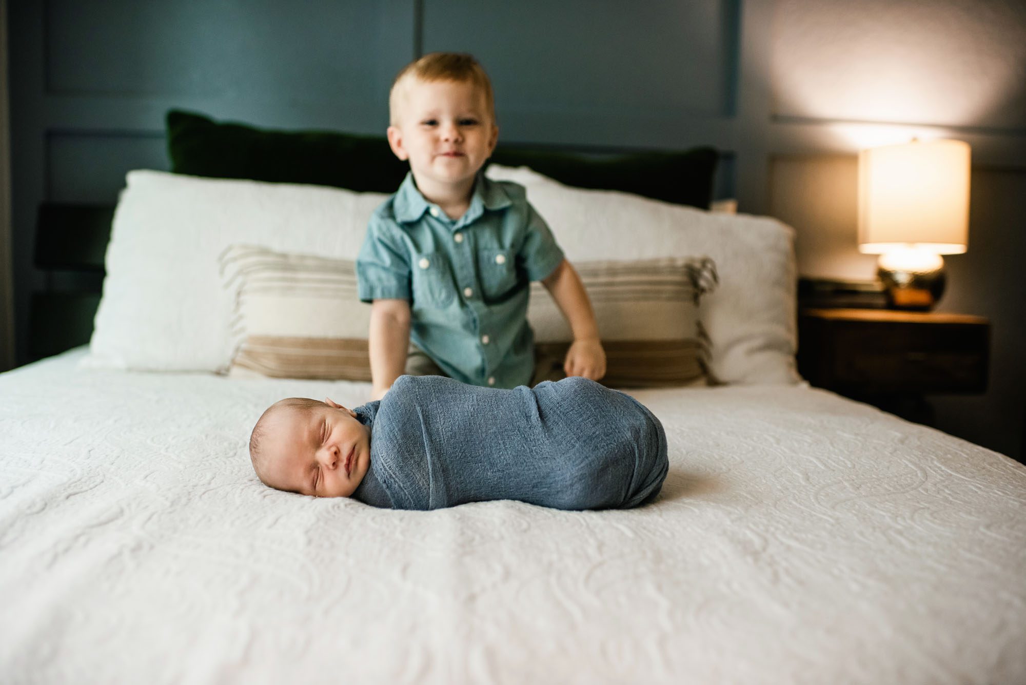 Big brother looking at newborn baby boy on bed, San Antonio newborn photographer