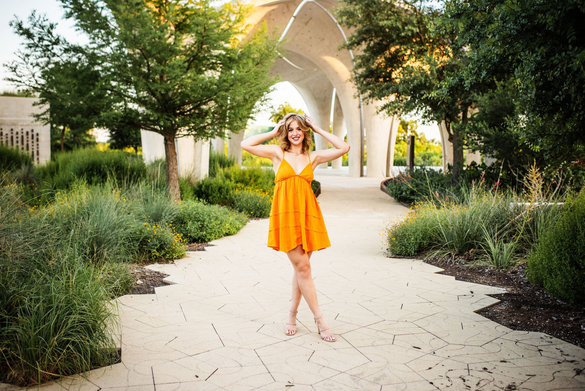 Senior in orange dress standing on path, San Antonio senior photography
