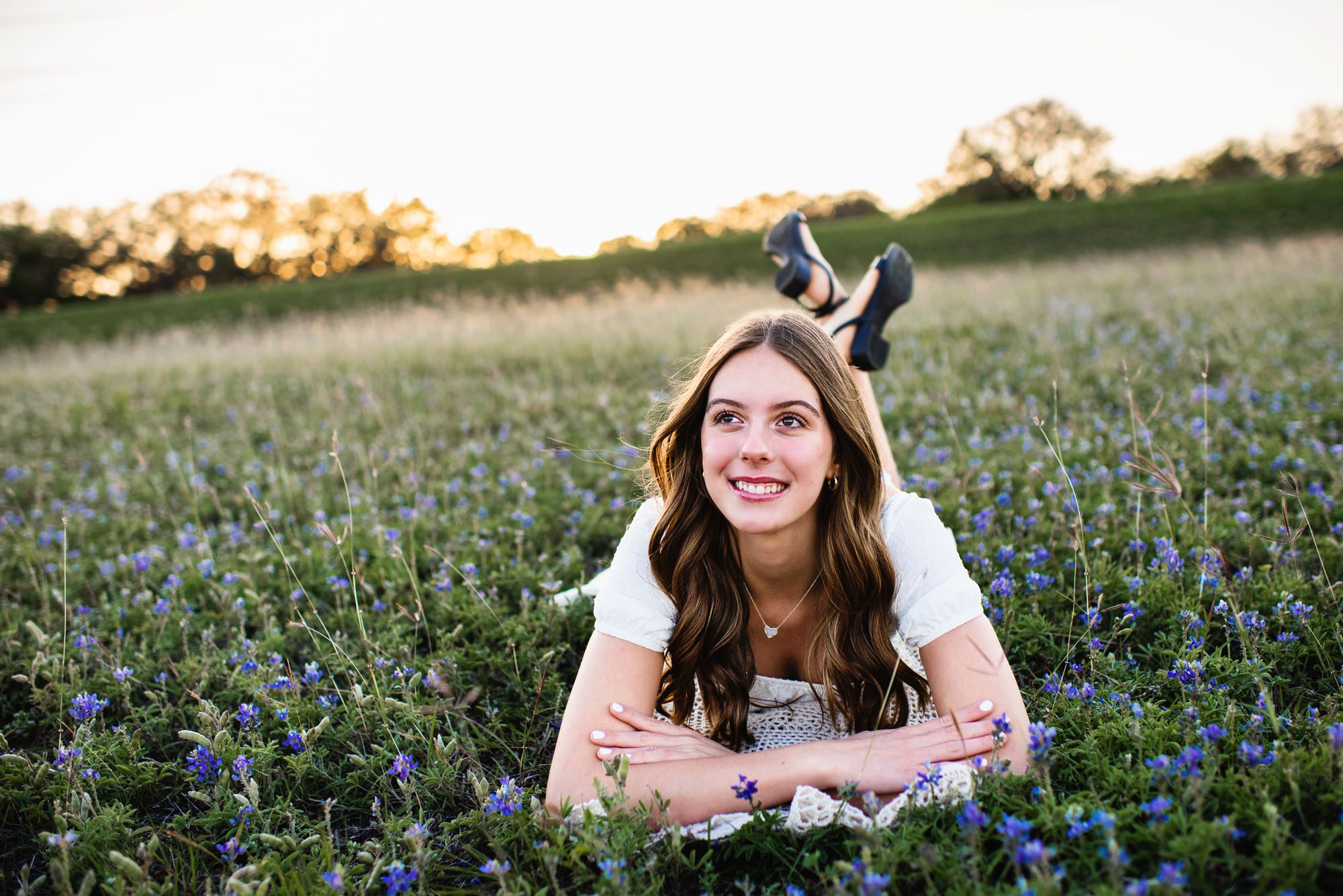 Girl in white dress laying in bluebonnet field, San Antonio senior photographer