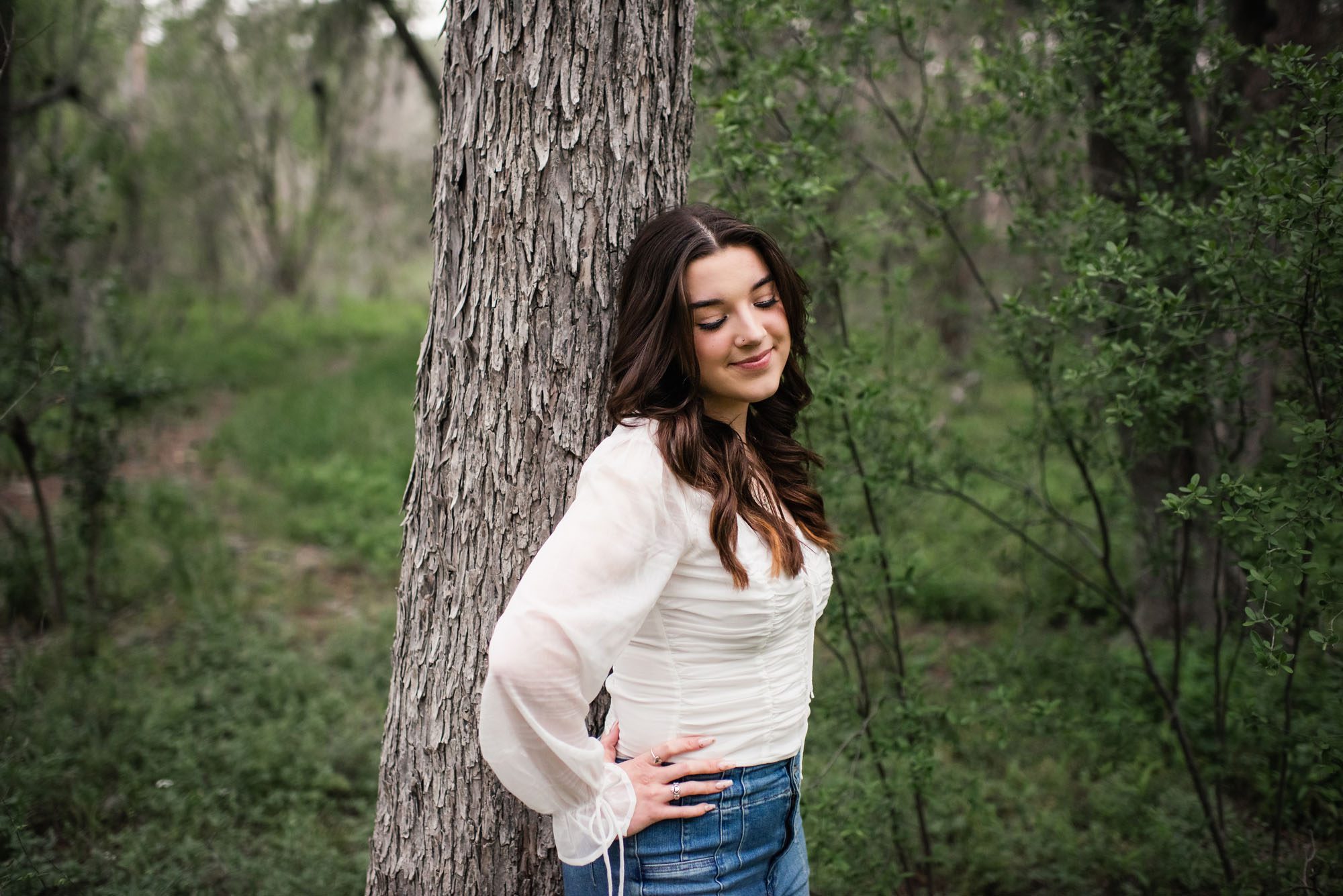 Girl in white shirt and jeans standing by tree looking down, San Antonio senior photographer