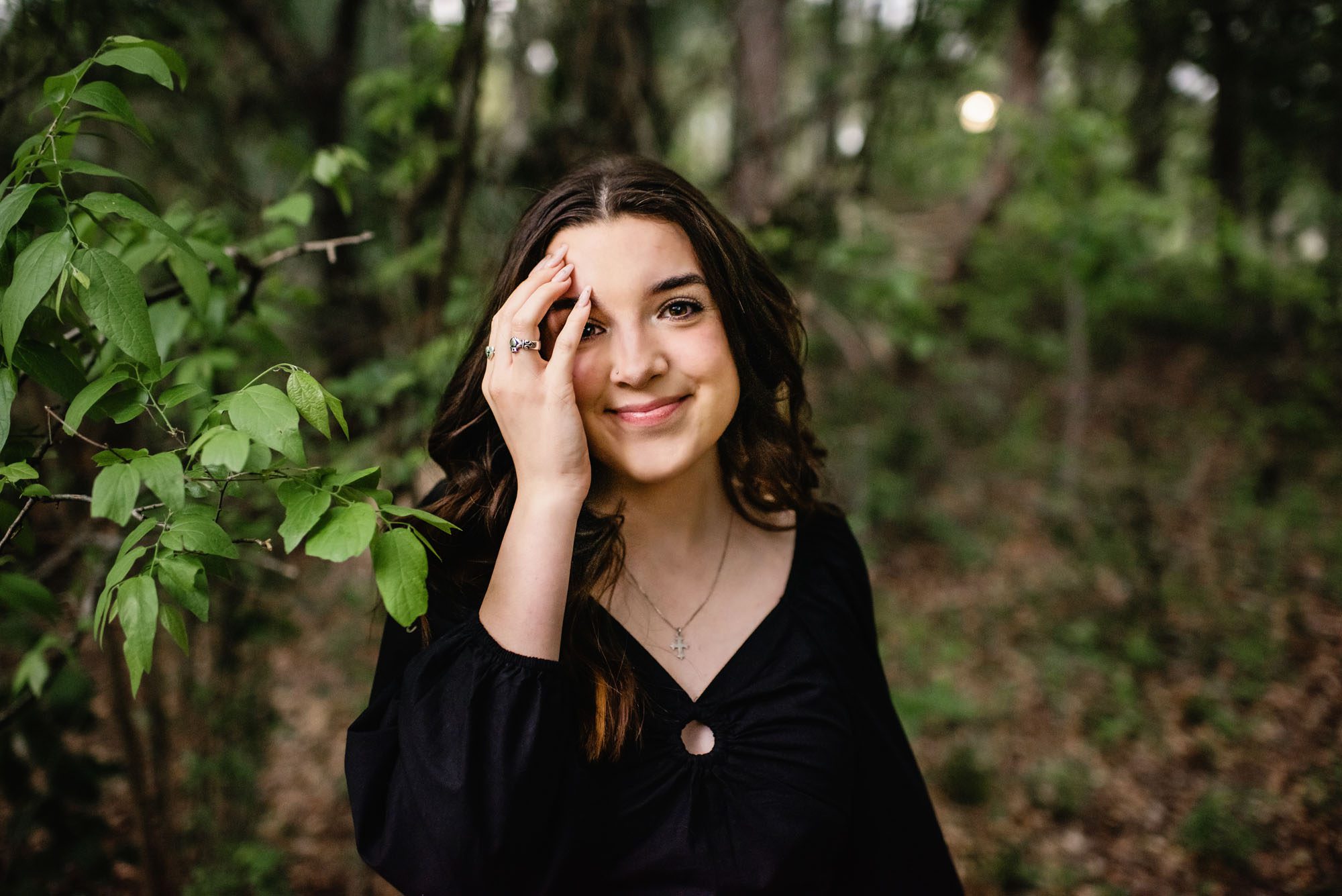 Girl standing by trees with hand covering face, San Antonio senior photographer