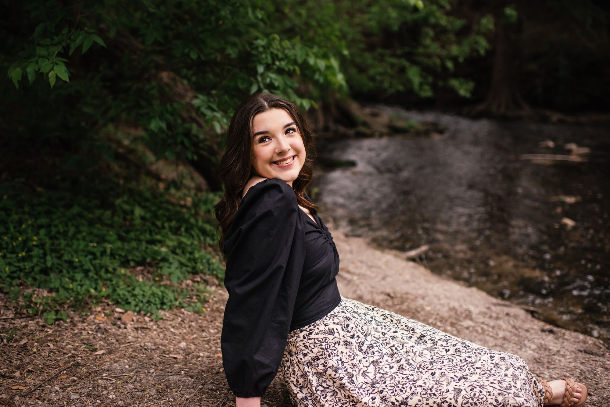 Girl sitting by creek looking over her shoulder and smiling, San Antonio senior photographer