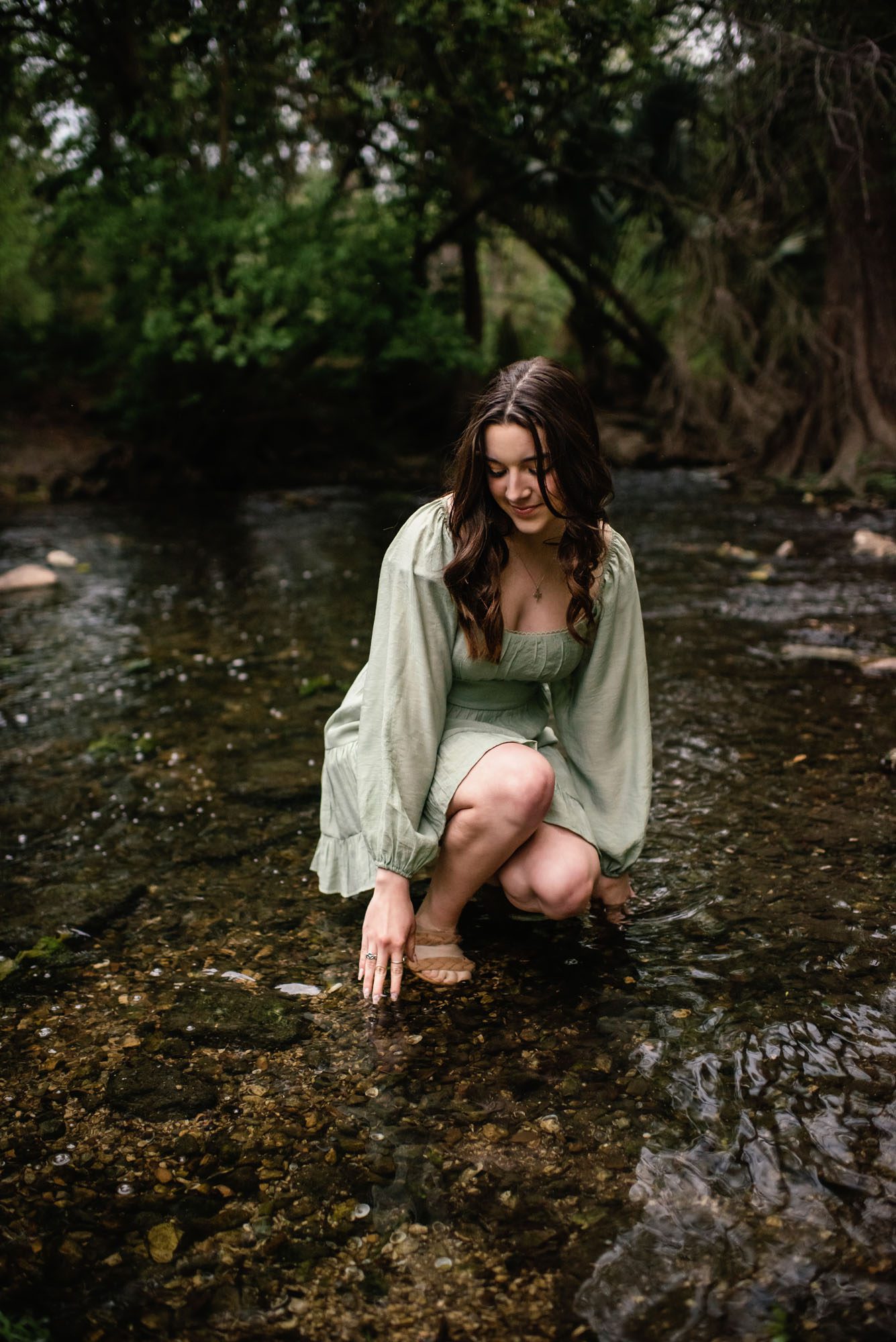 Girl kneeling down touching the shallow creek water, San Antonio senior photographer