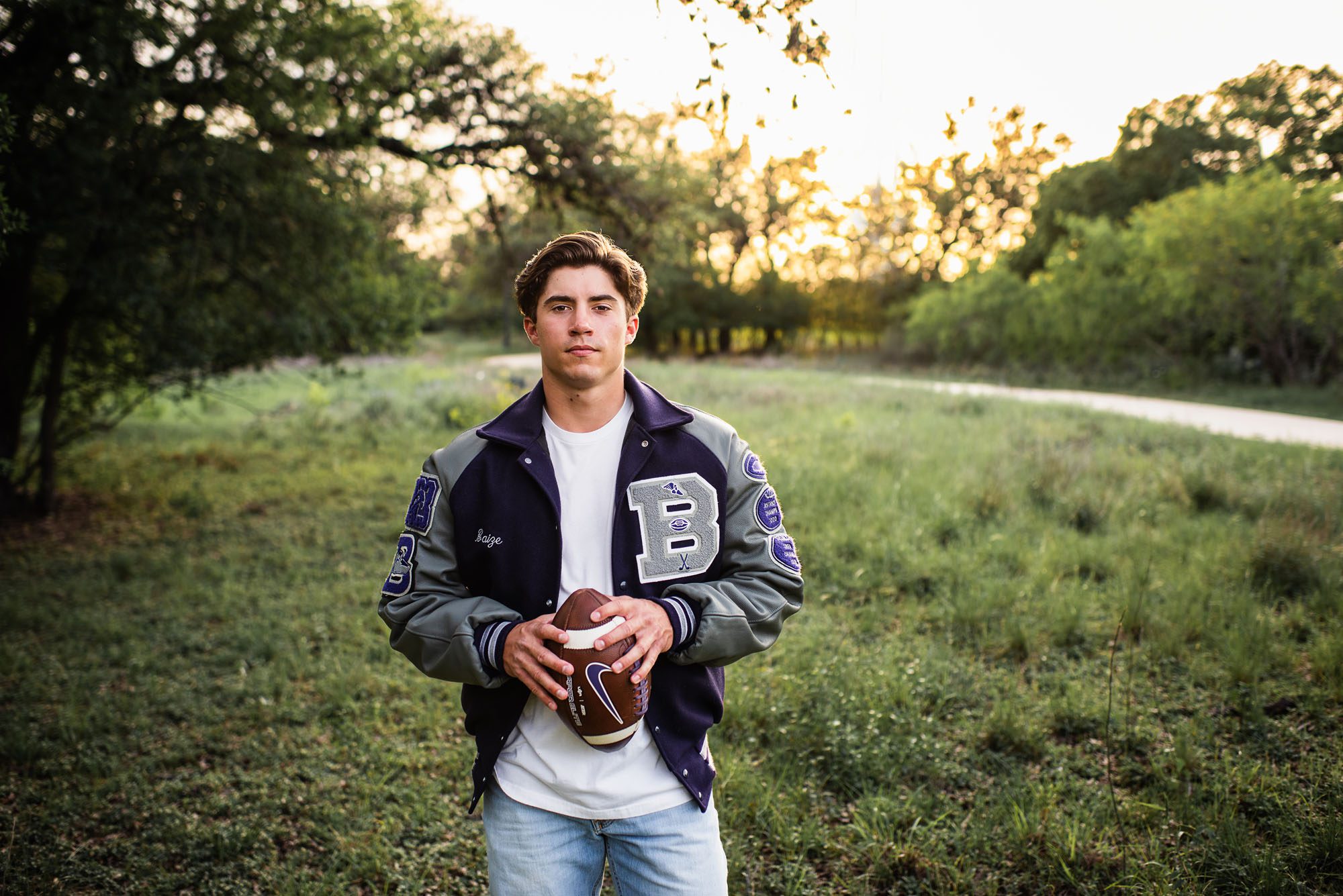 Boy holding football with letter jacket at sunset, San Antonio senior photographer