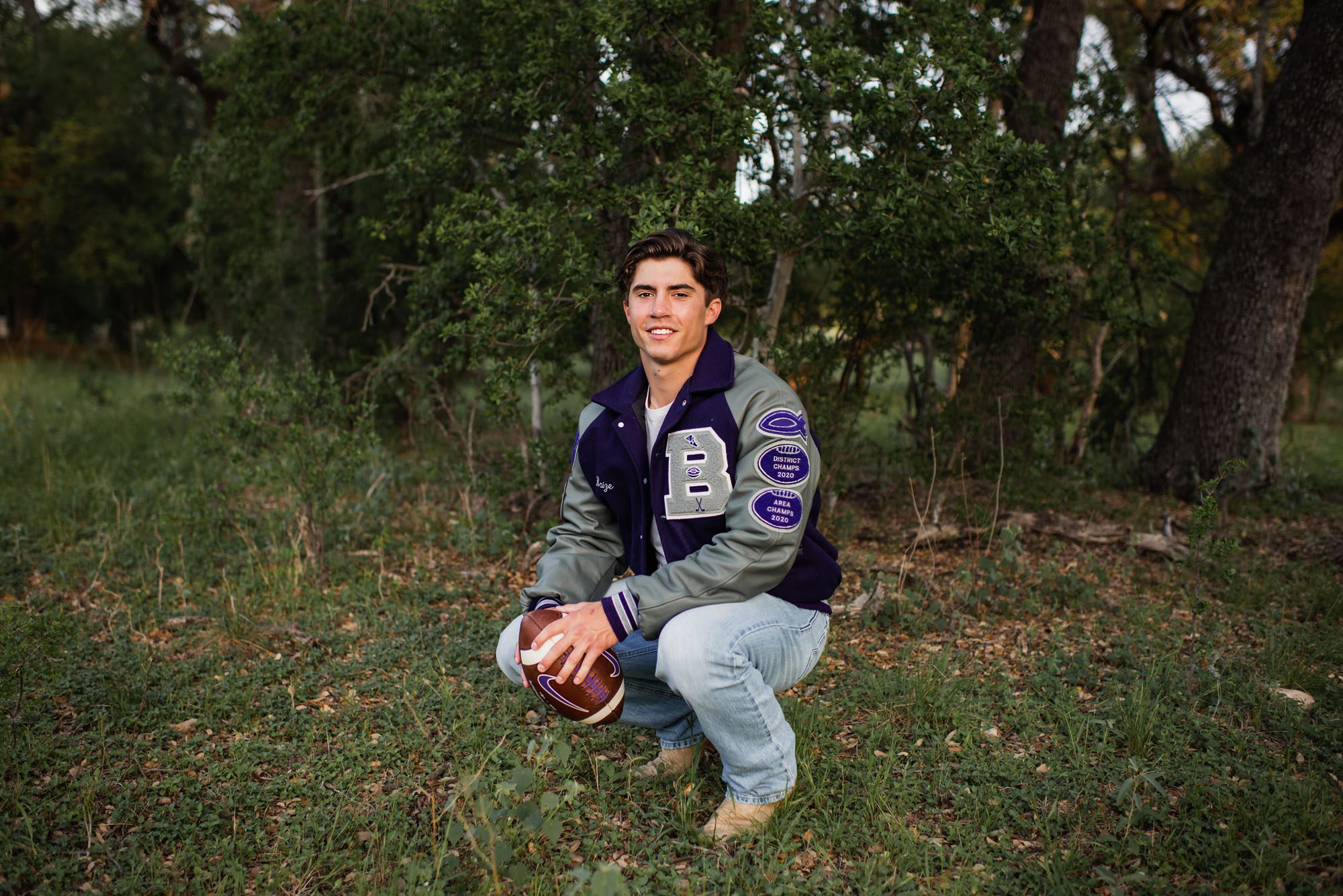 Boy squatting down with football and letter jacket, San Antonio senior photographer