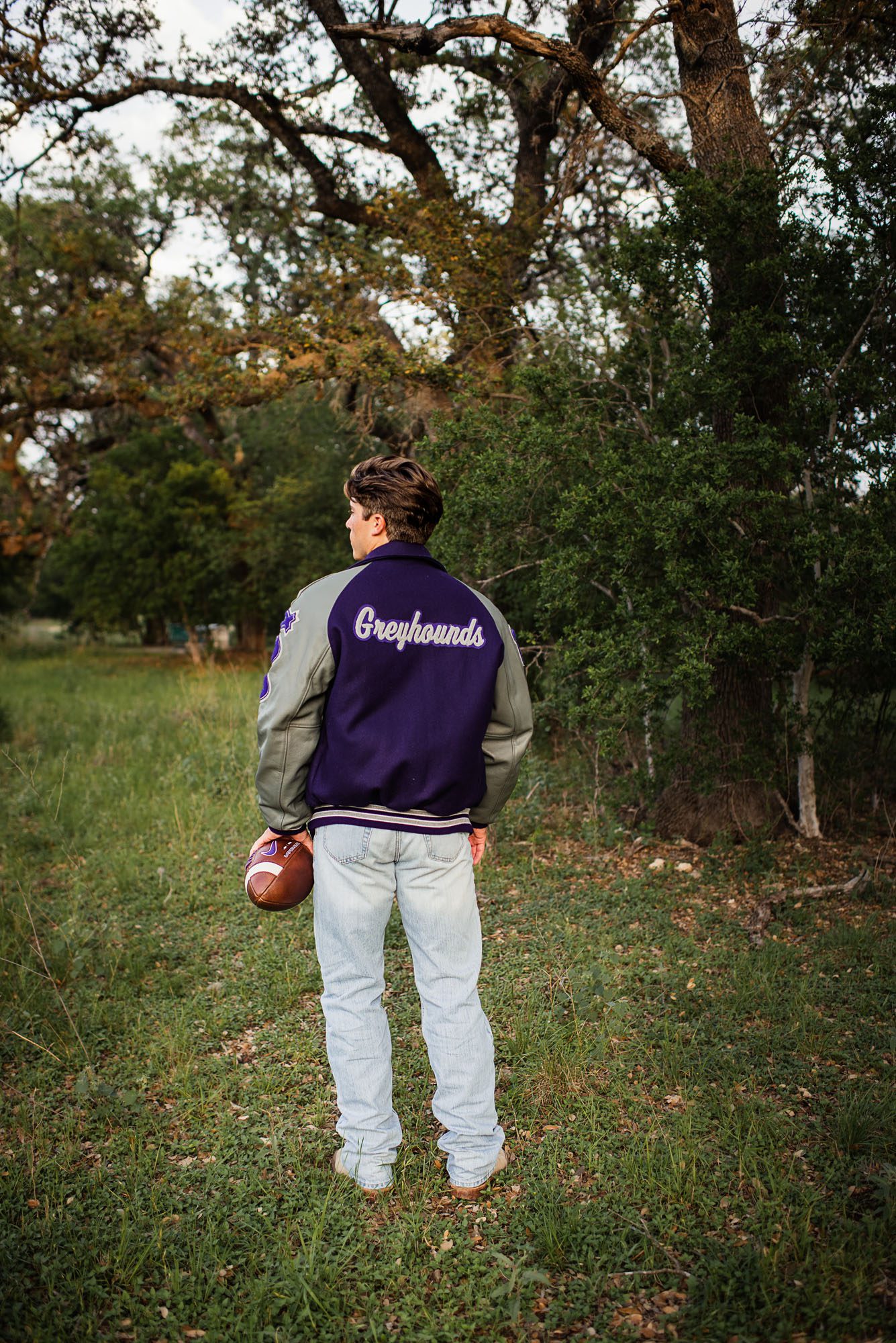 Boy standing with football and letter jacket, San Antonio senior photographer
