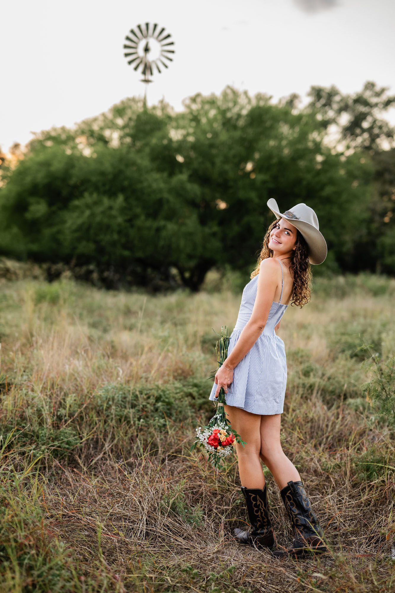 High school girl standing in field by windmill, San Antonio senior photographer