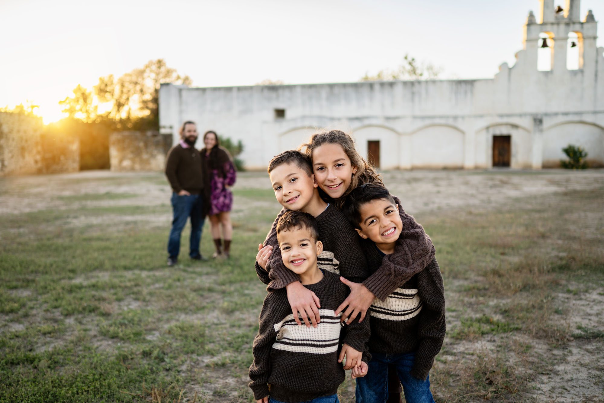 Four children hugging with parents and white building in background; San Antonio family photographer